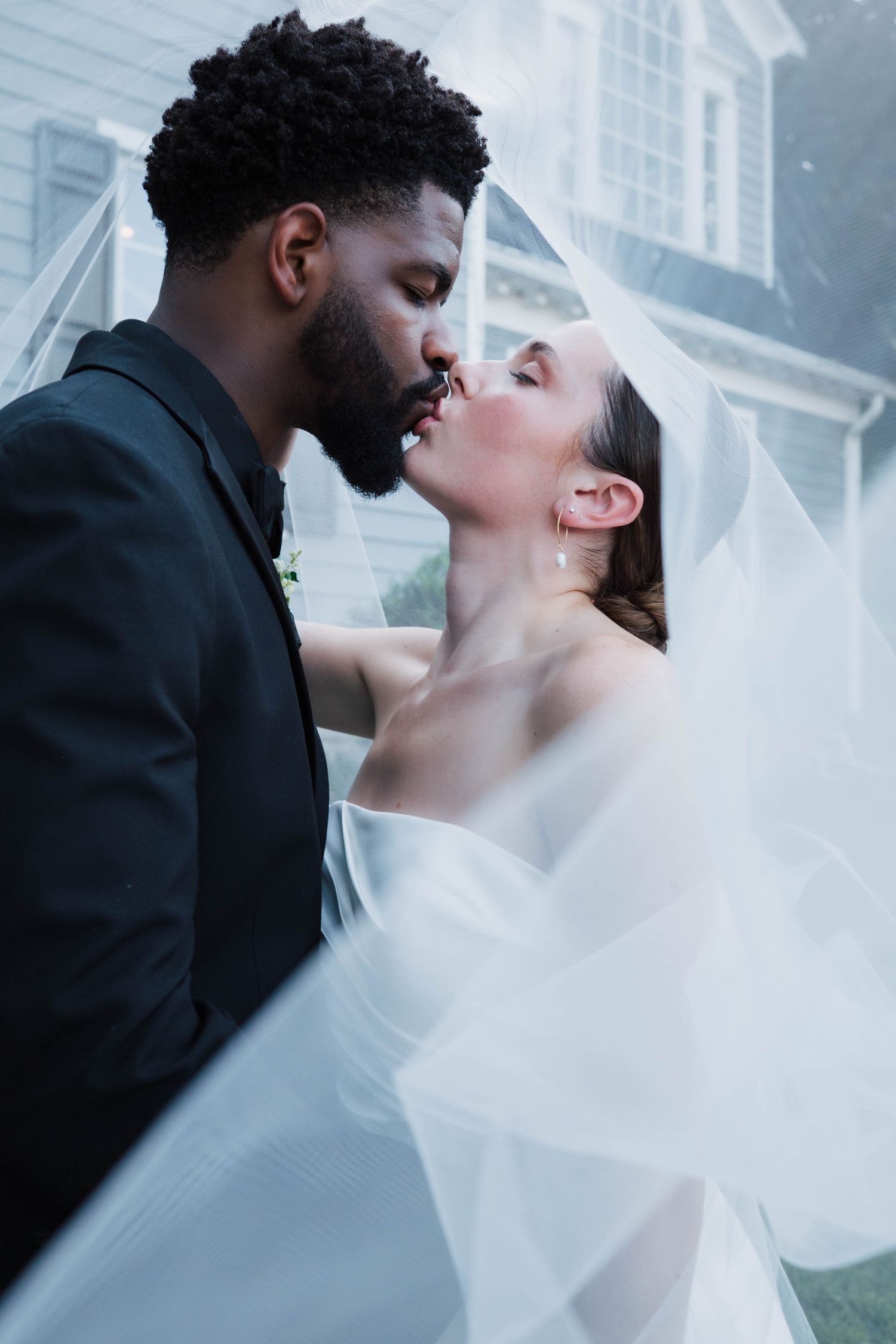 Bride and groom sharing an intimate kiss beneath her flowing veil on their wedding day