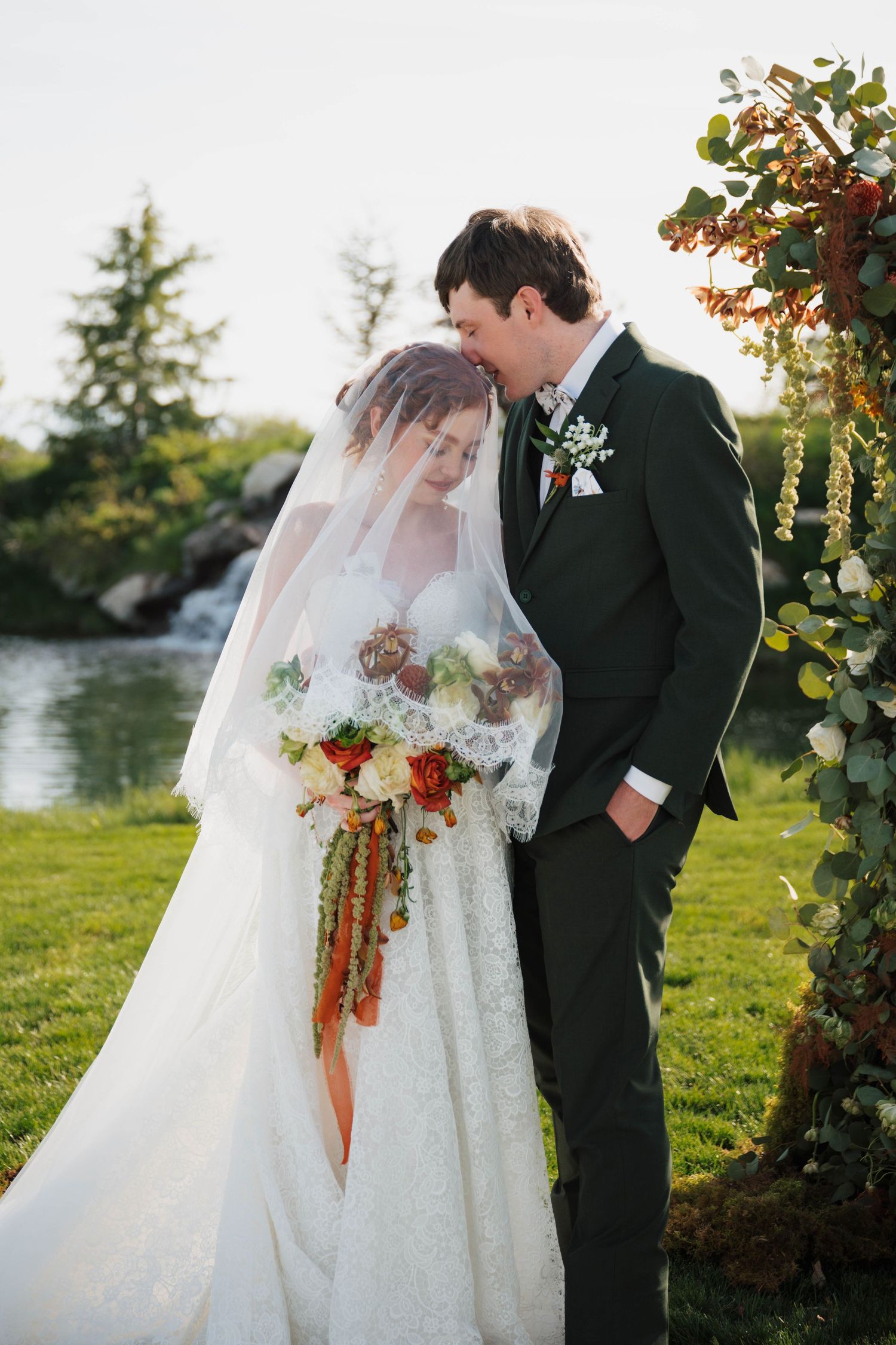 Bride and groom share tender moment at outdoor wedding ceremony with a floral arch at mint barrel barn in nampa, idaho