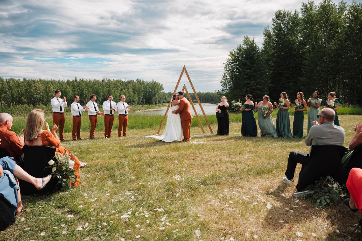 An outdoor wedding ceremony with wedding party and guests gathered under blue skies.