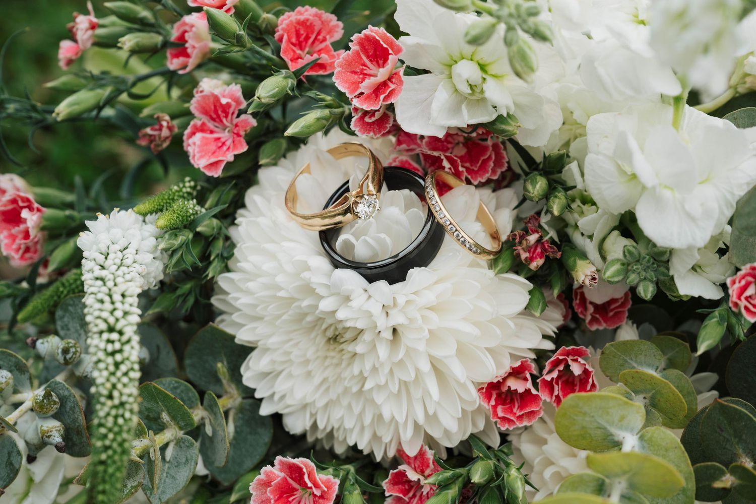 Wedding rings nestled among white and pink flowers in a romantic floral arrangement.