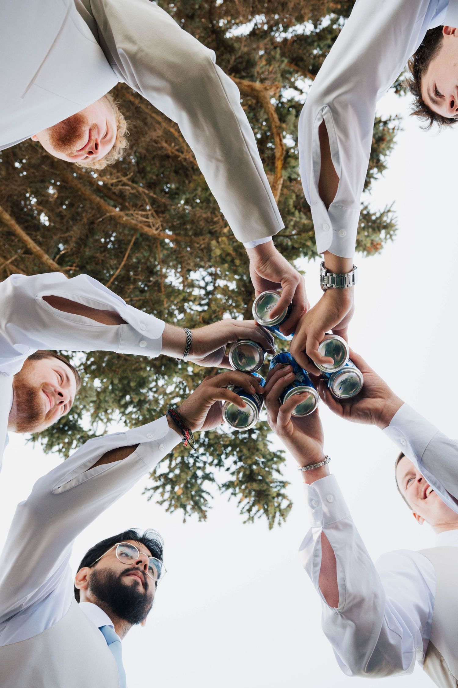Groomsmen in white shirts cheering and raising beer cans in a creative circular photo composition.