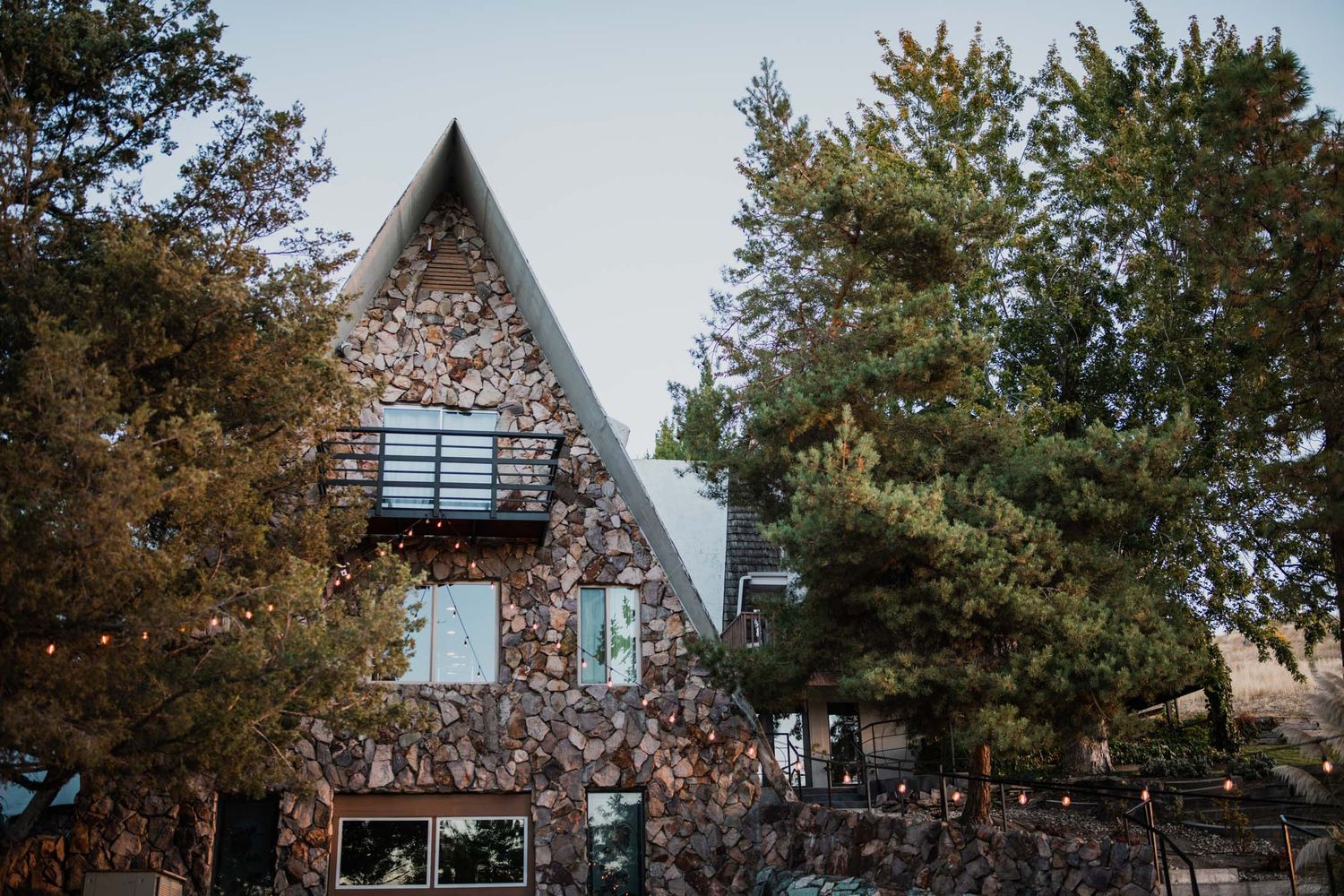 A series of A-frame cabins nestled among autumn trees with string lights creating a cozy outdoor atmosphere.
