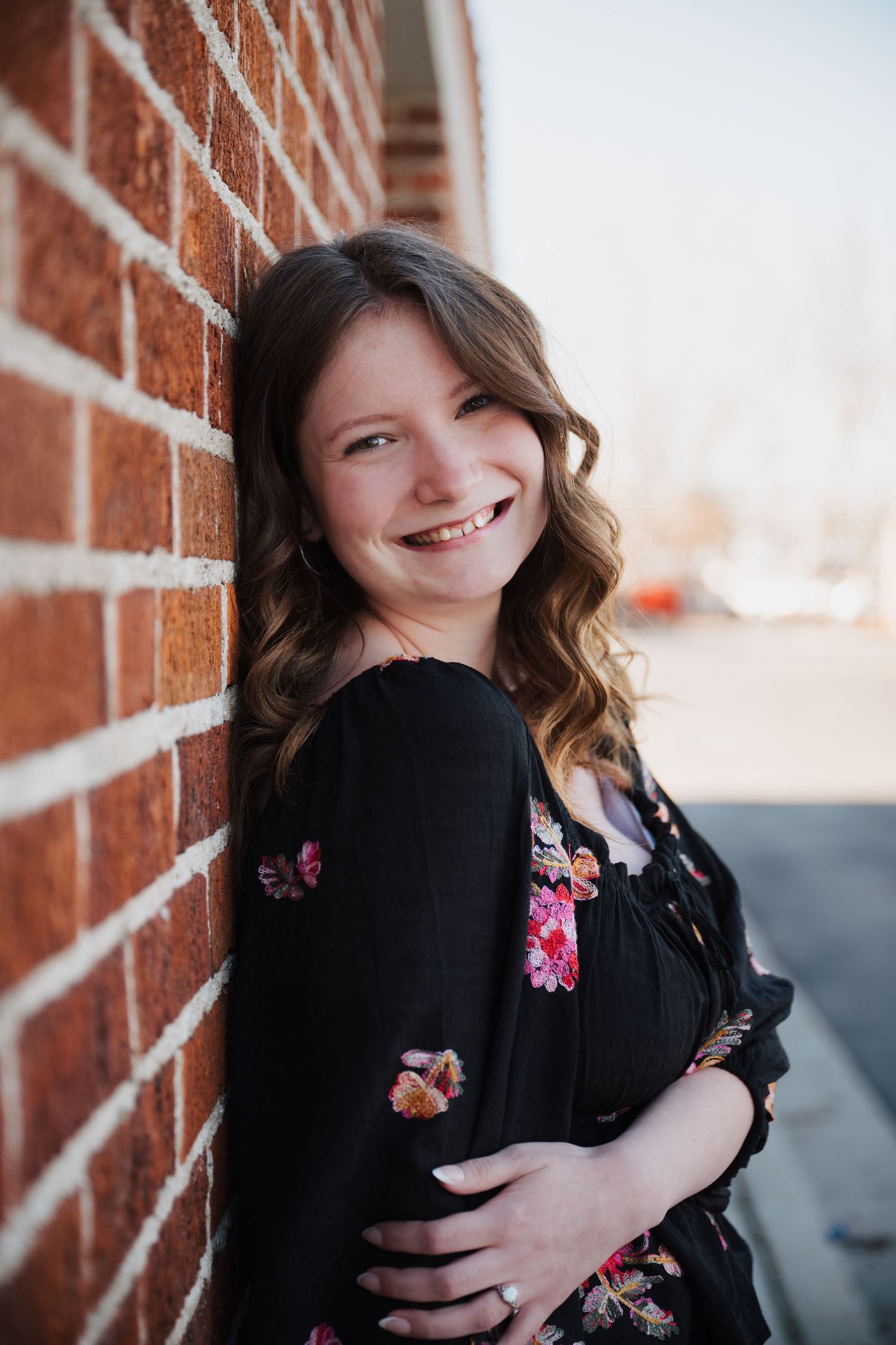 Casual portrait session against red brick wall in black floral outfit.