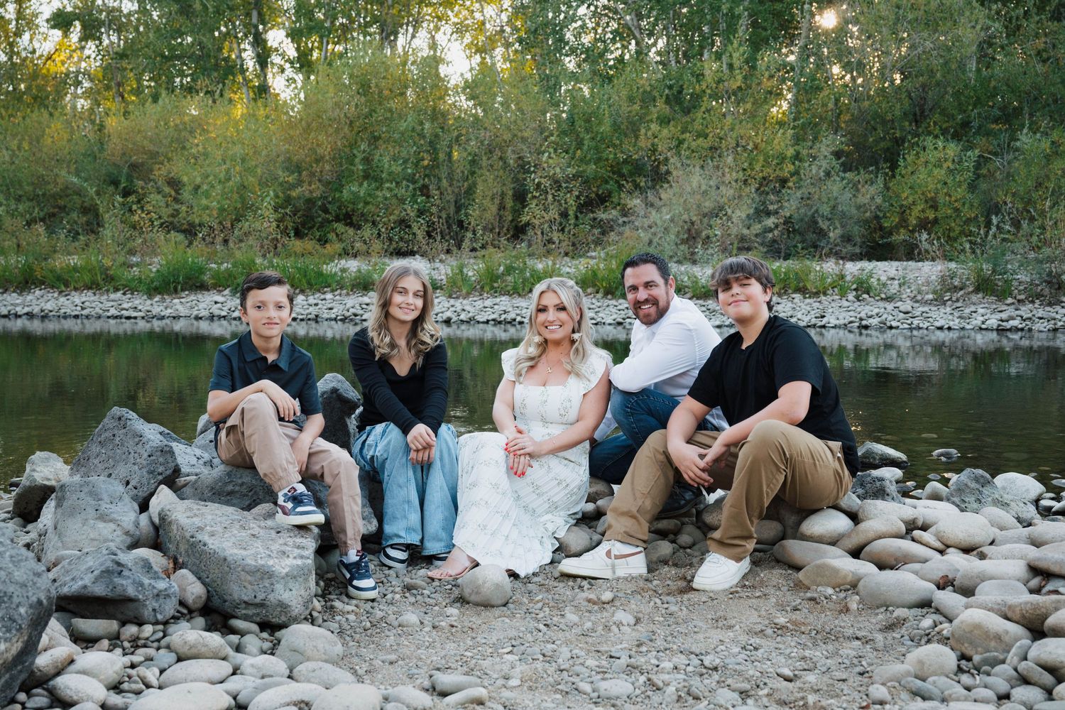 Family members relaxing on rocky riverbank during outdoor photo session.