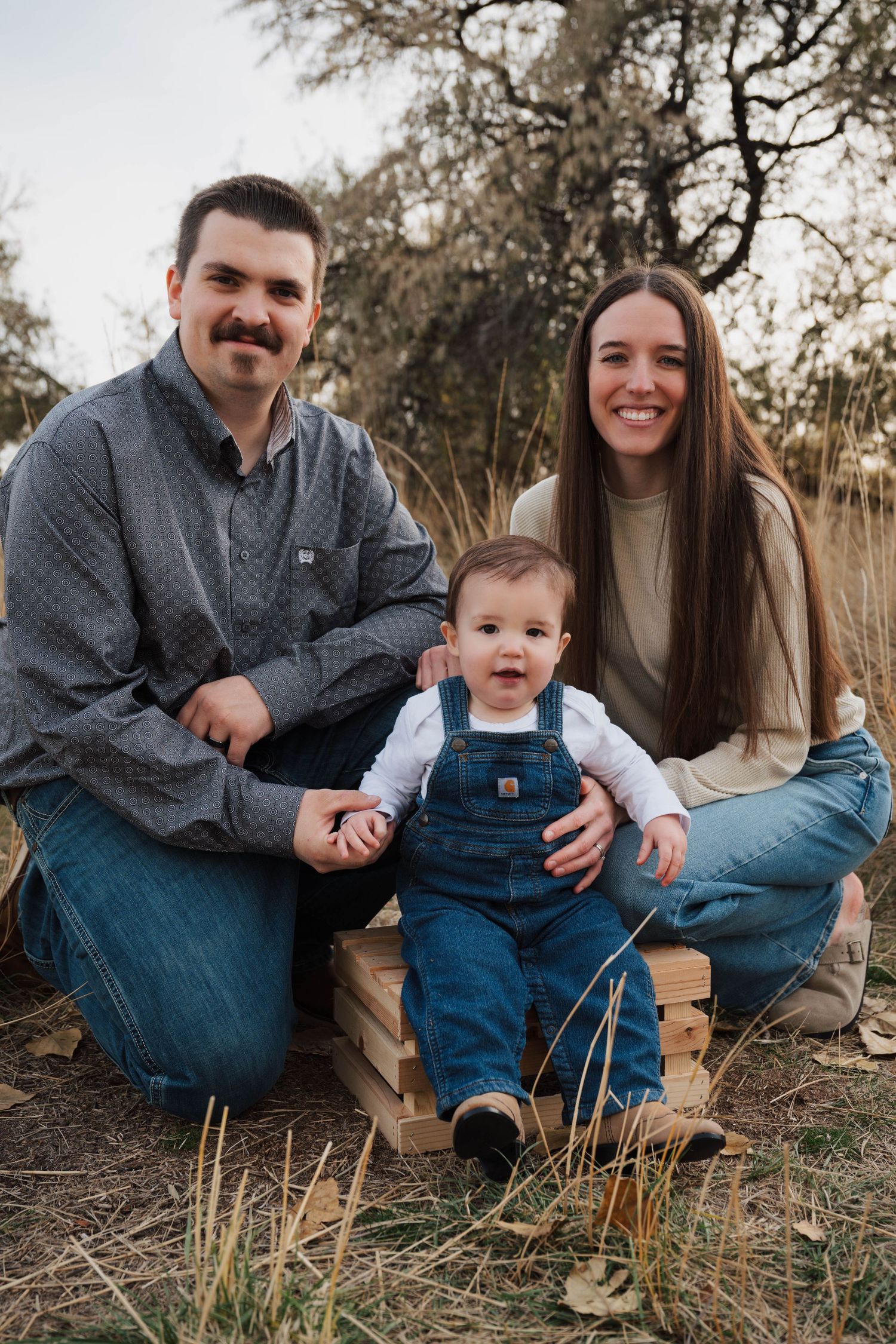 Family sitting together in outdoor field with tall grass during golden hour photo session.