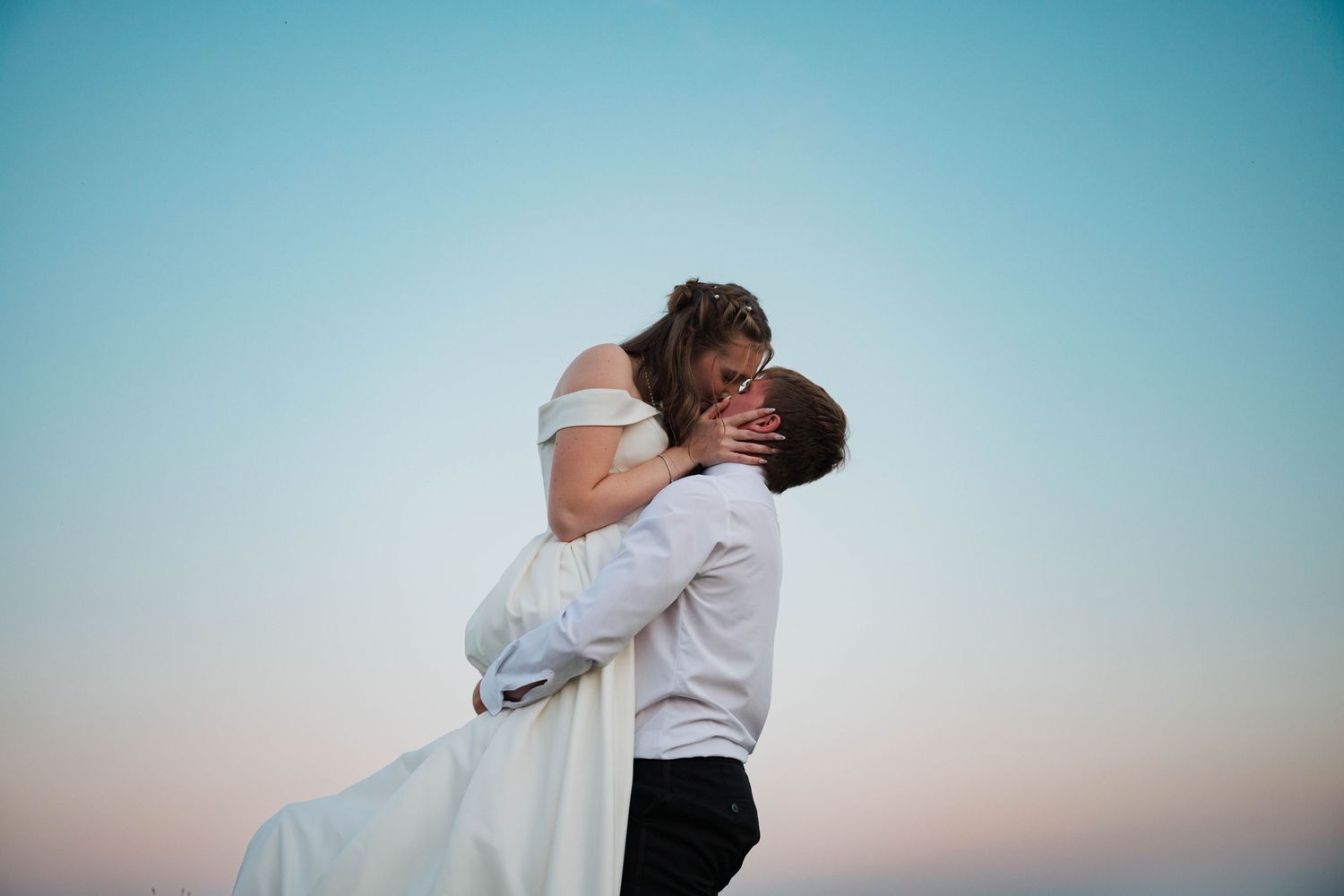 A romantic sunset embrace between newlyweds against a blue sky.