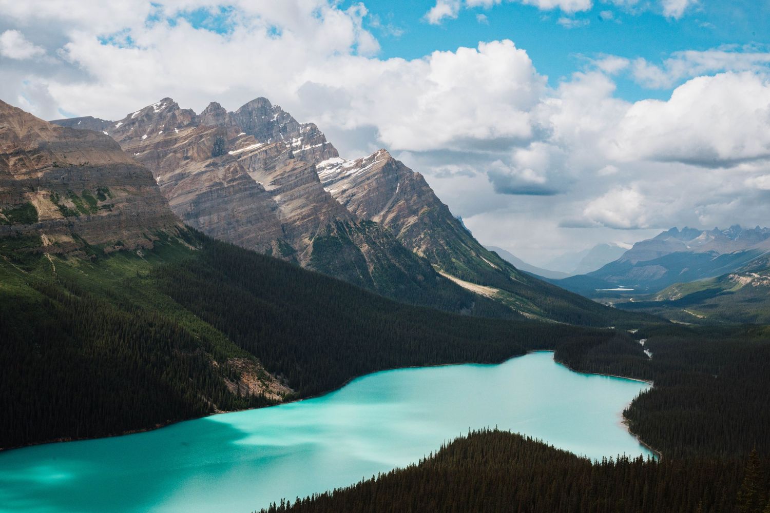 Panoramic view of turquoise Peyto Lake surrounded by Canadian Rocky Mountains under cloudy sky.
