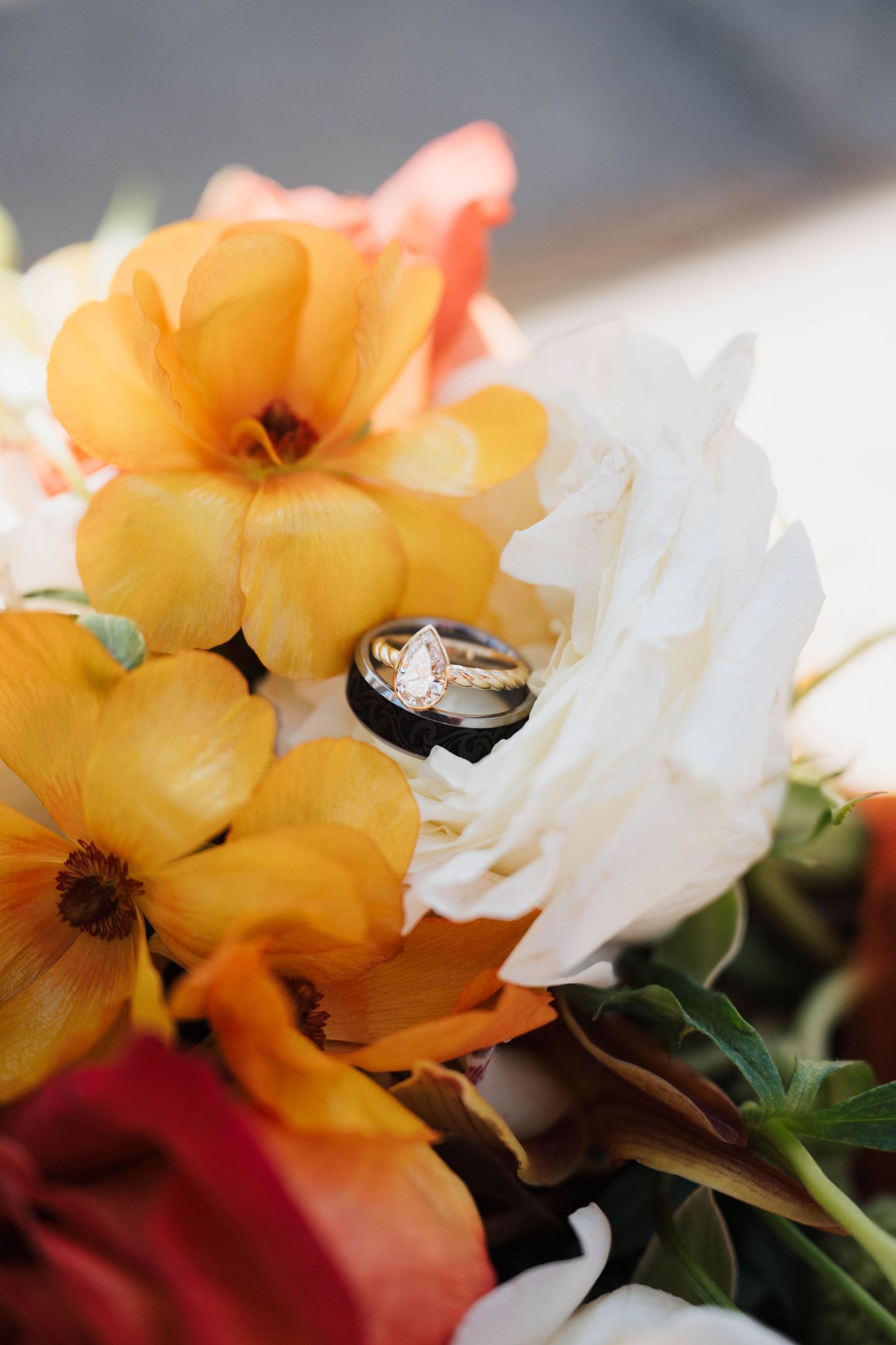 Wedding rings resting on a vibrant bouquet of orange, yellow, and white flowers.
