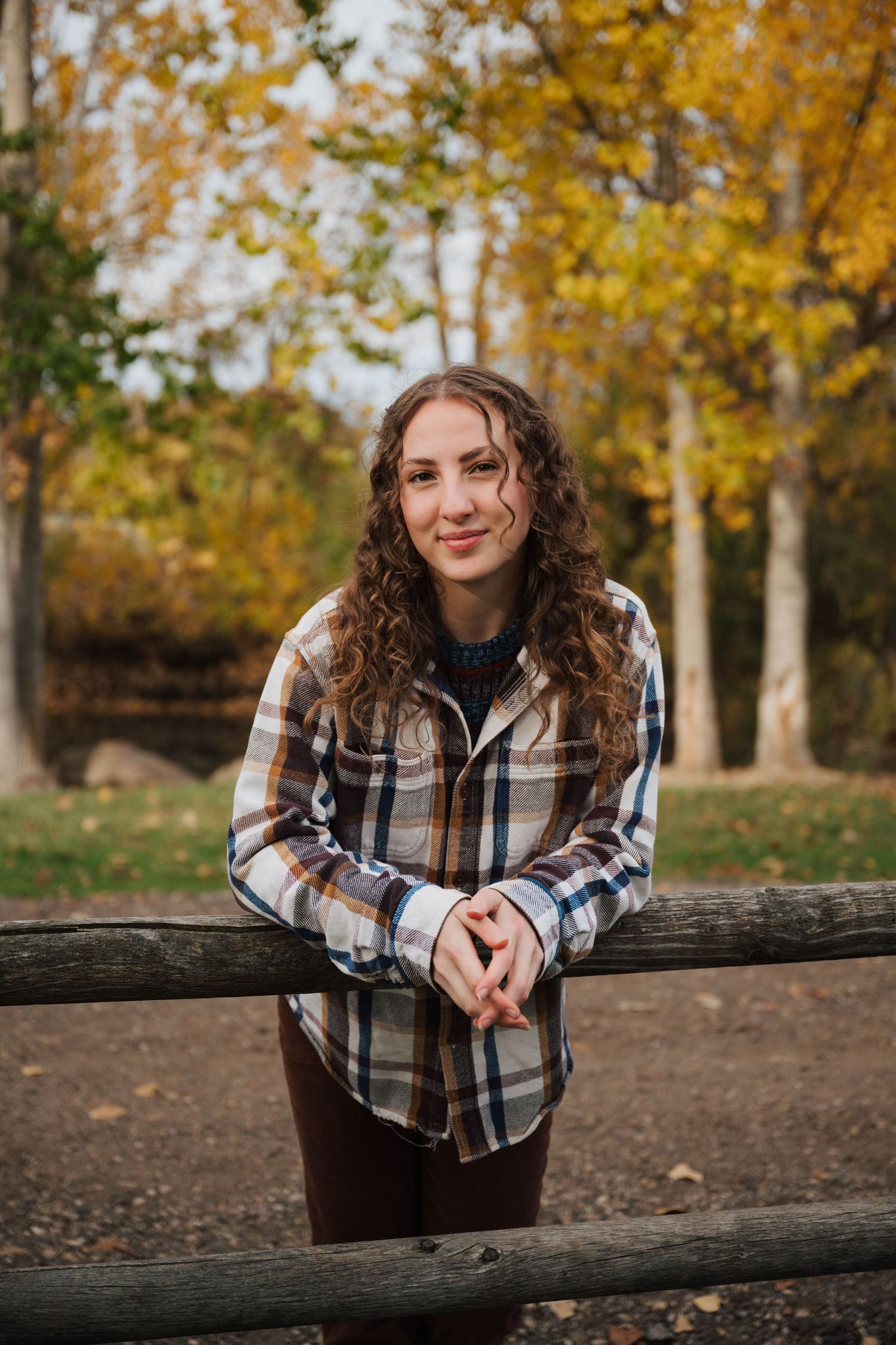 Casual outdoor photo shoot with rustic wooden fence and golden fall foliage.