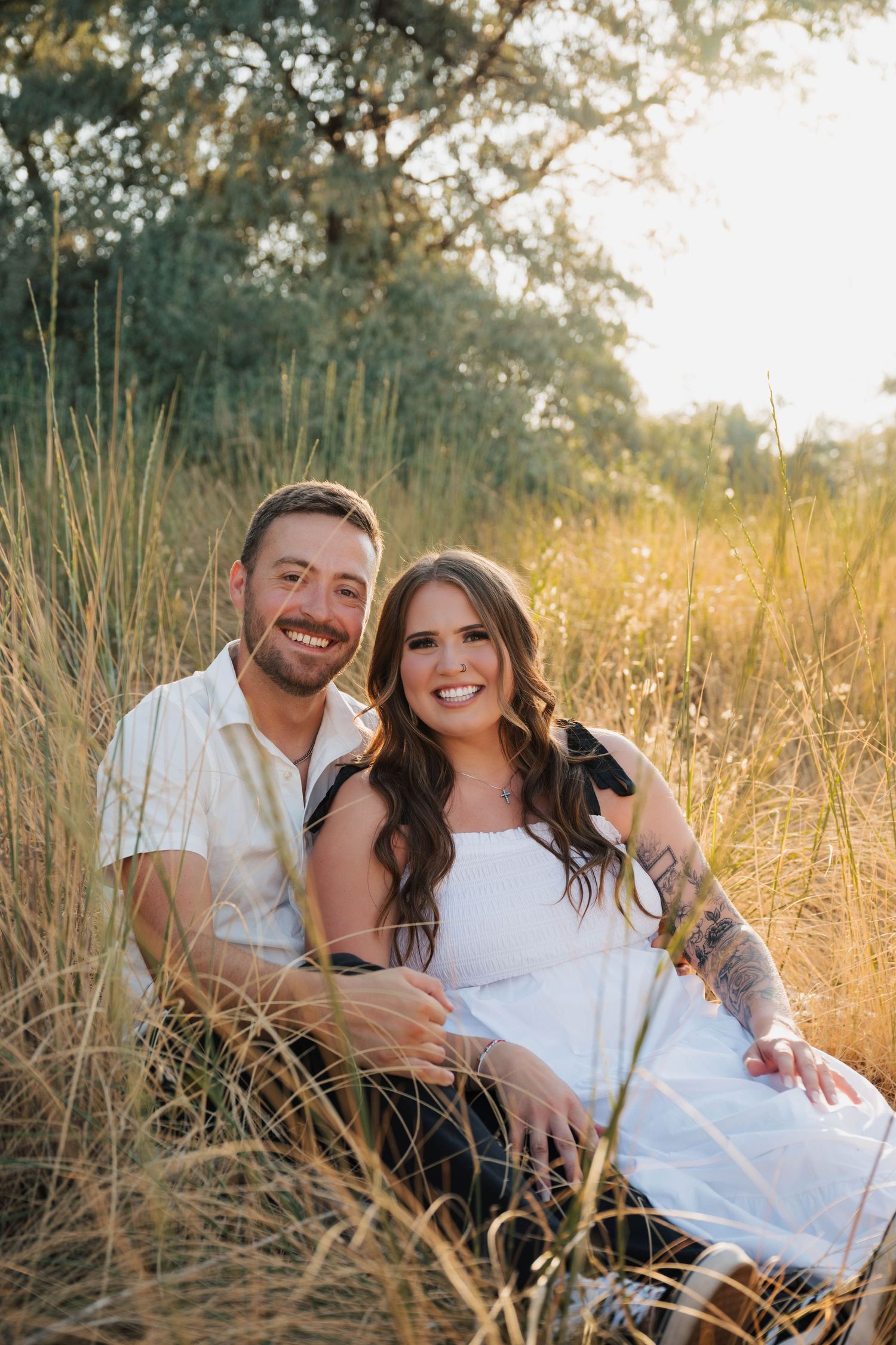 Couple lounging together in golden tall grass during sunset photography session.