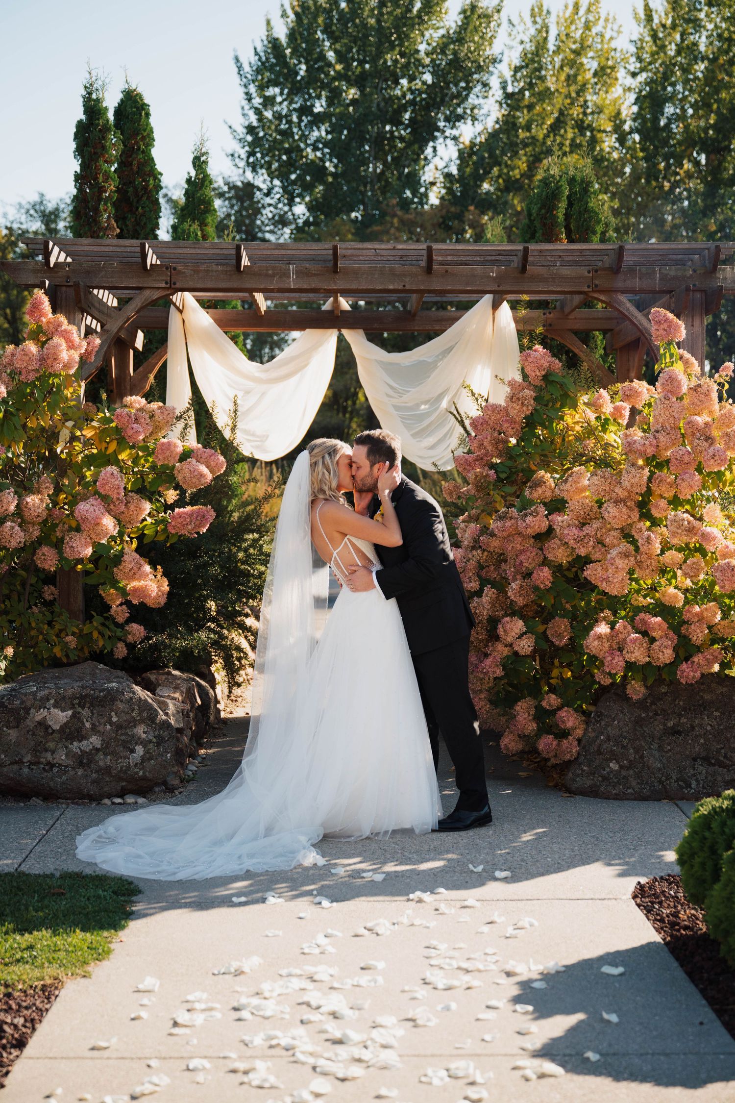 Wedding ceremony space decorated with pink roses and white fabric against garden backdrop.