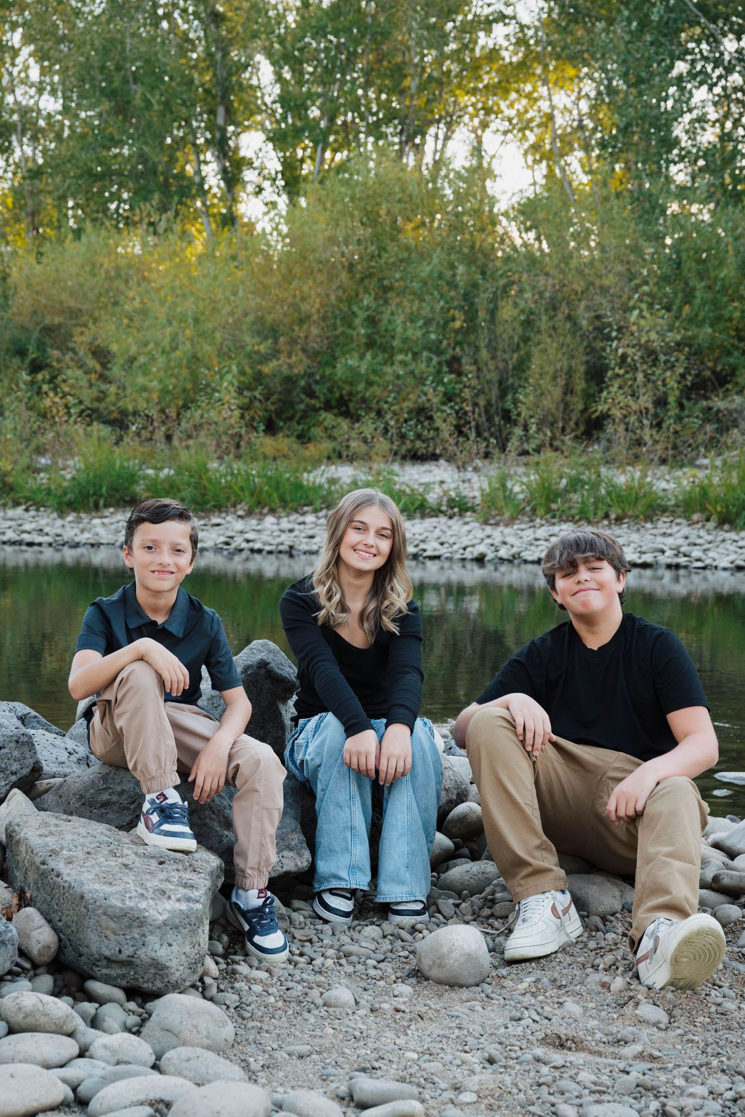 Group sitting casually on rocky riverbank during sunset photoshoot.