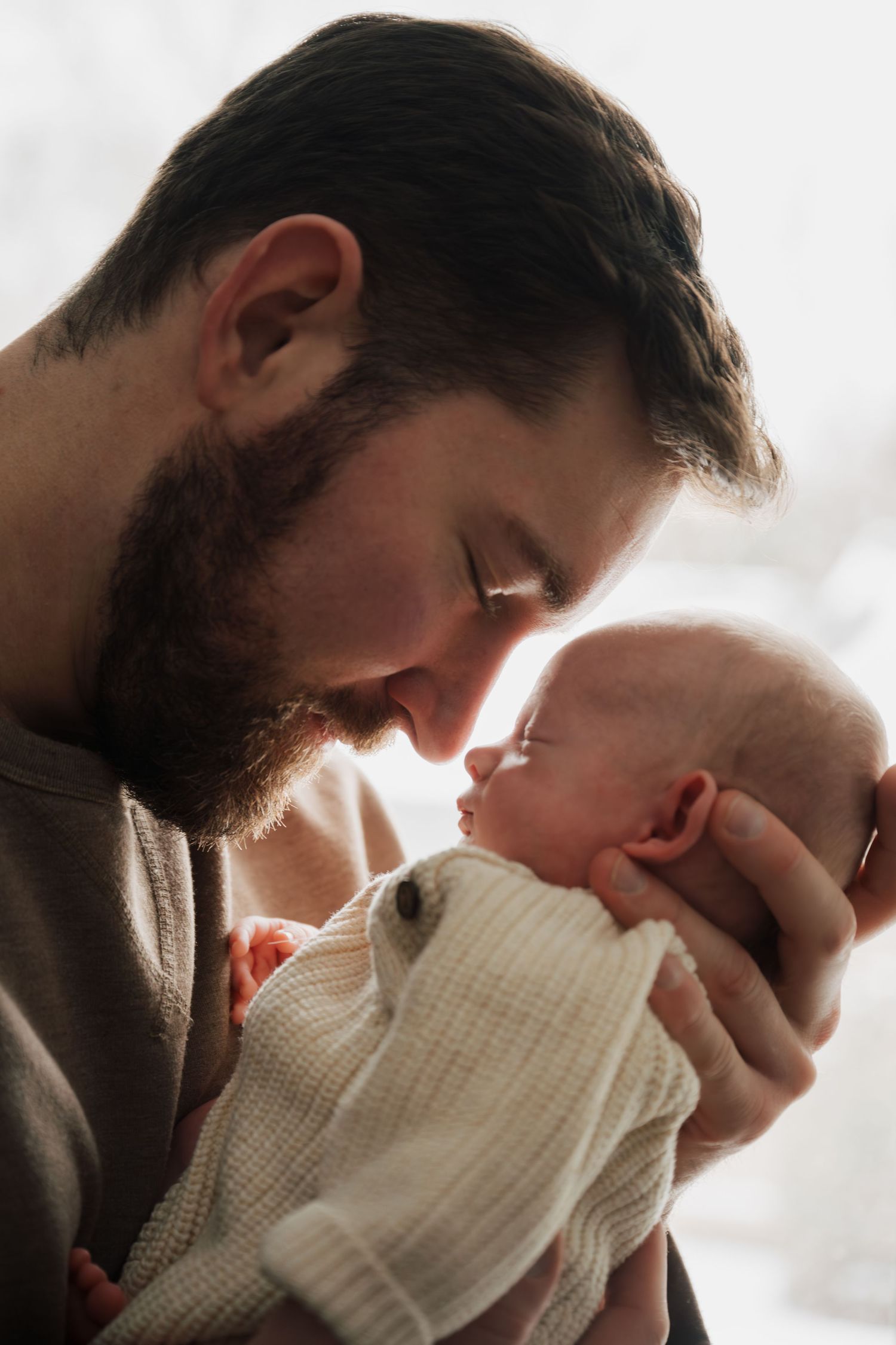 Intimate close-up of parents bonding with newborn in soft window light.
