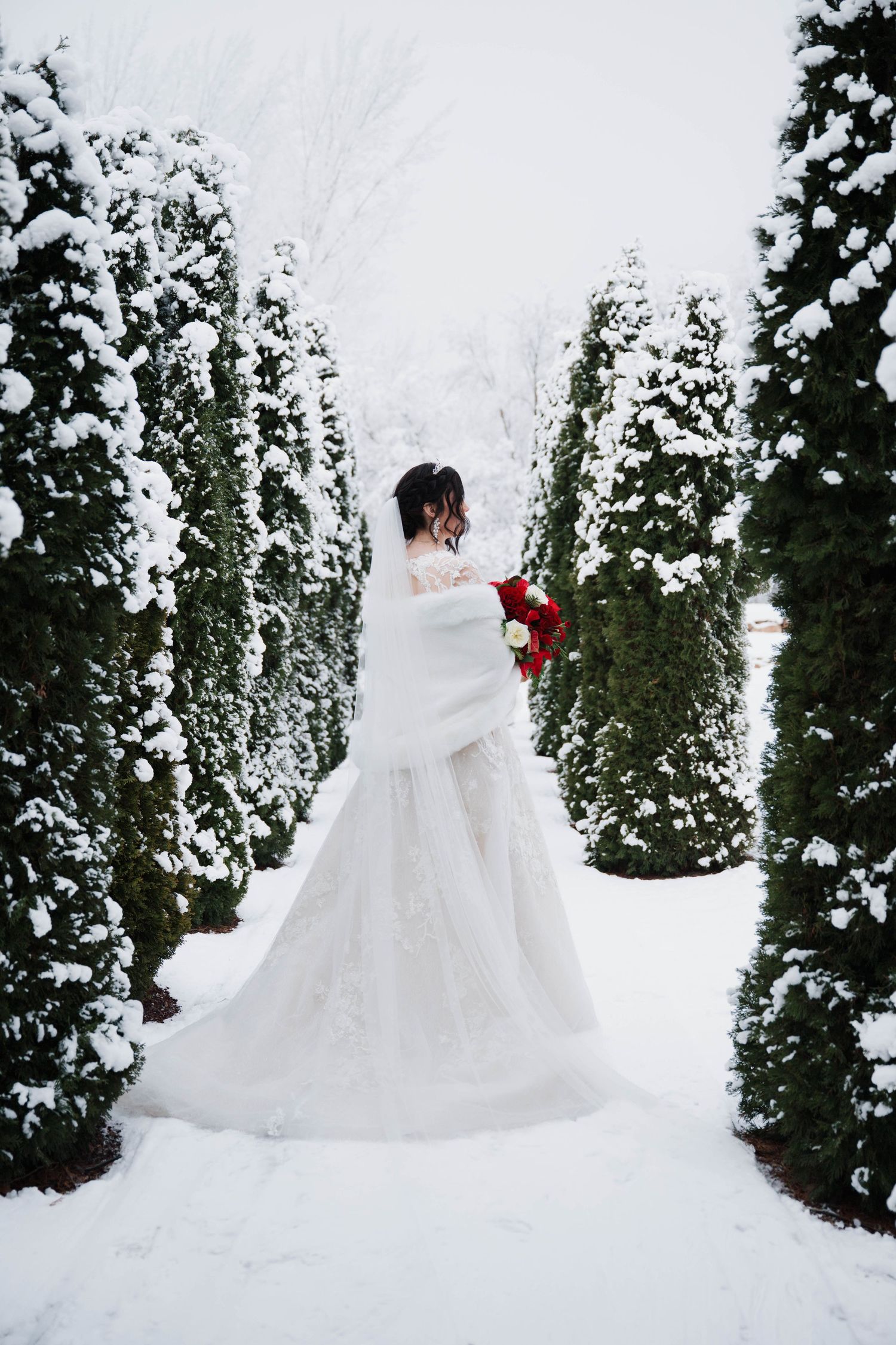 Bride holding a red bouquet in a snowy winter garden at Chateau des Fleurs wedding venue in Eagle, Idaho