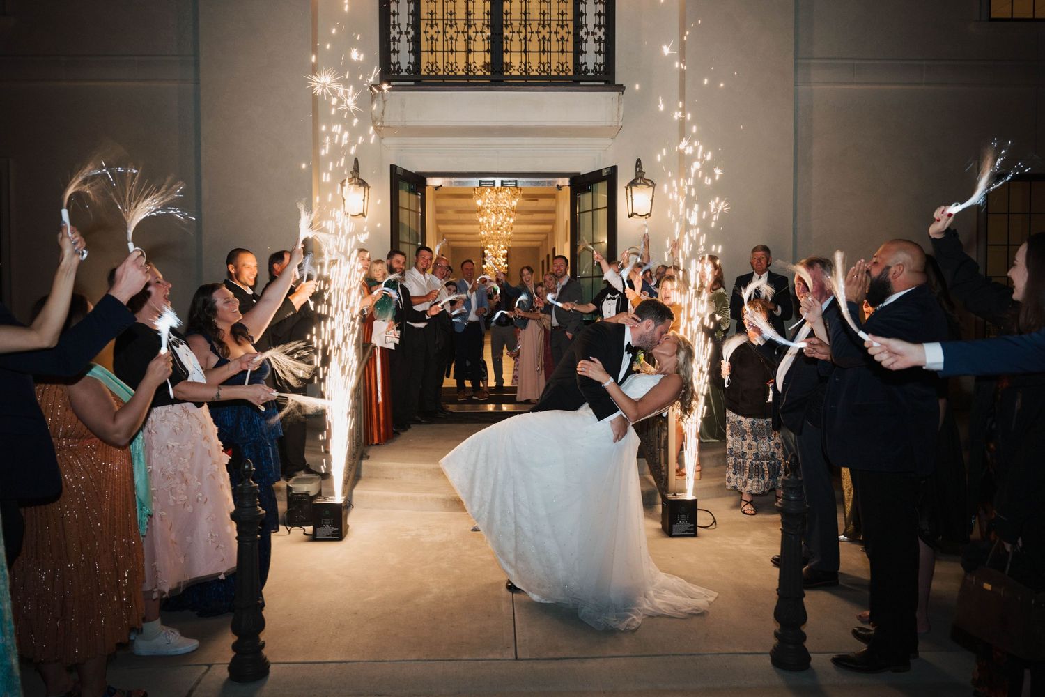 Wedding guests line a hallway with sparklers as a couple makes their grand exit at an elegant indoor venue.