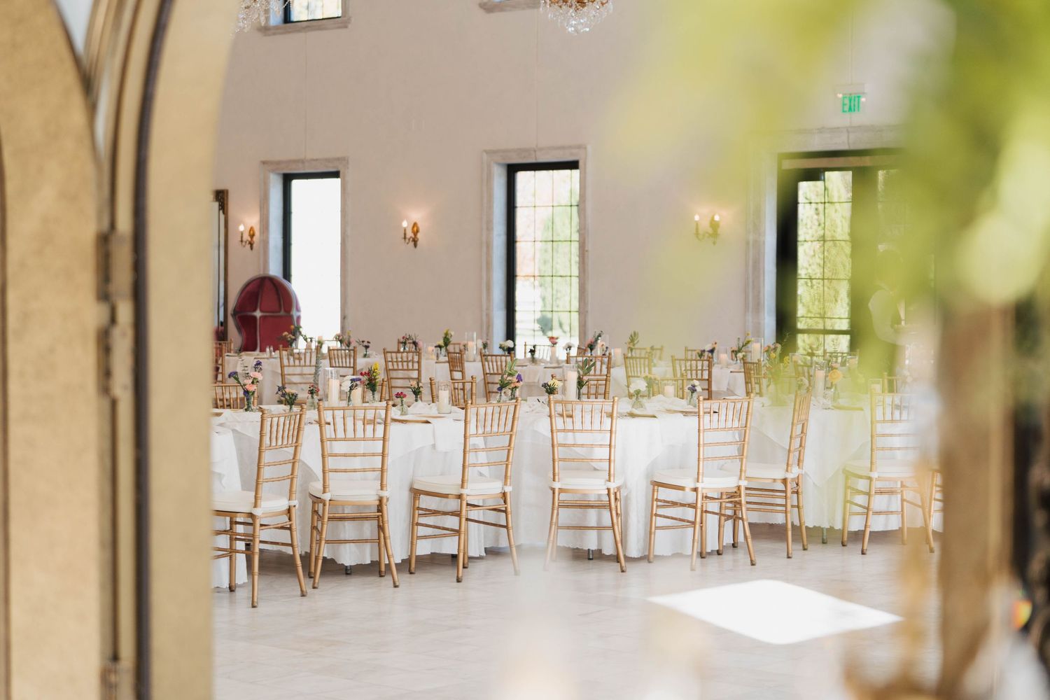 A bright and airy wedding reception venue with white chiavari chairs arranged in rows around elegant dining tables.