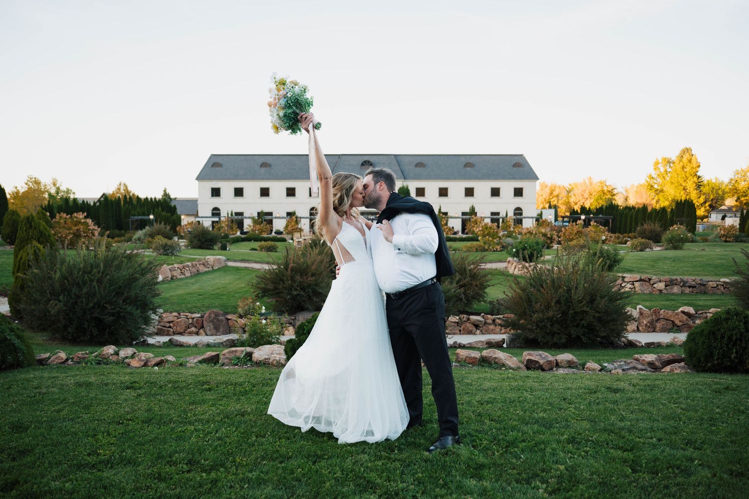 A couple celebrates their wedding on a beautiful lawn with white barns and autumn trees in the background.