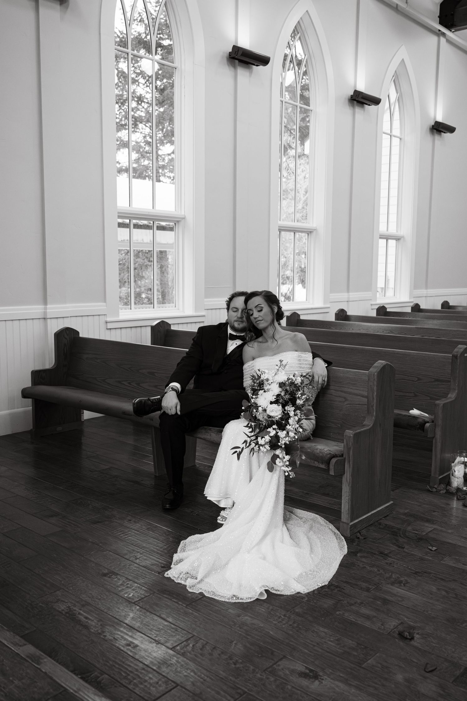 A white wedding dress flows across dark wooden floors in an empty chapel with wooden pews.
