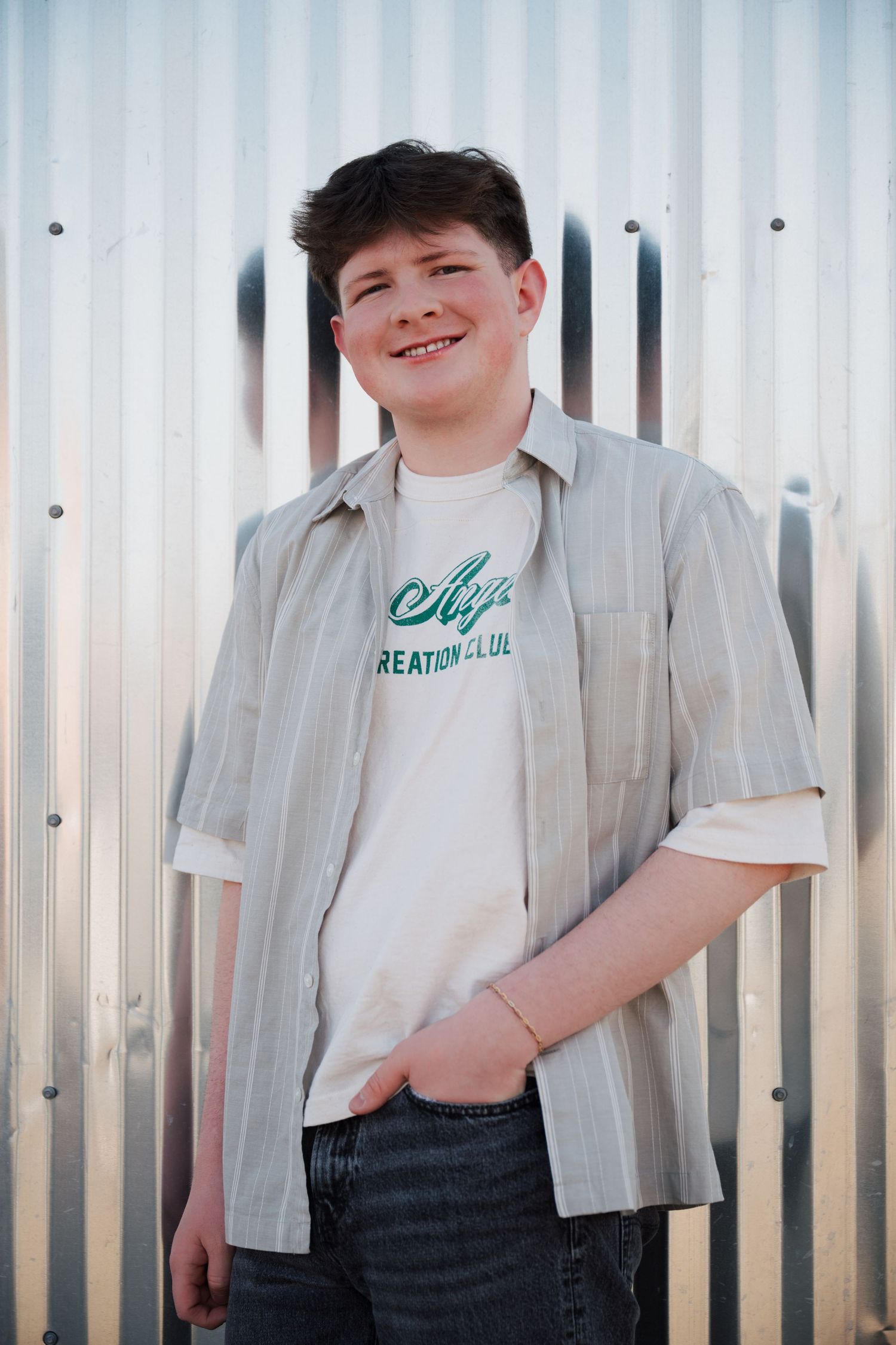 Portrait against metal siding wearing a casual button-up shirt over a graphic tee.