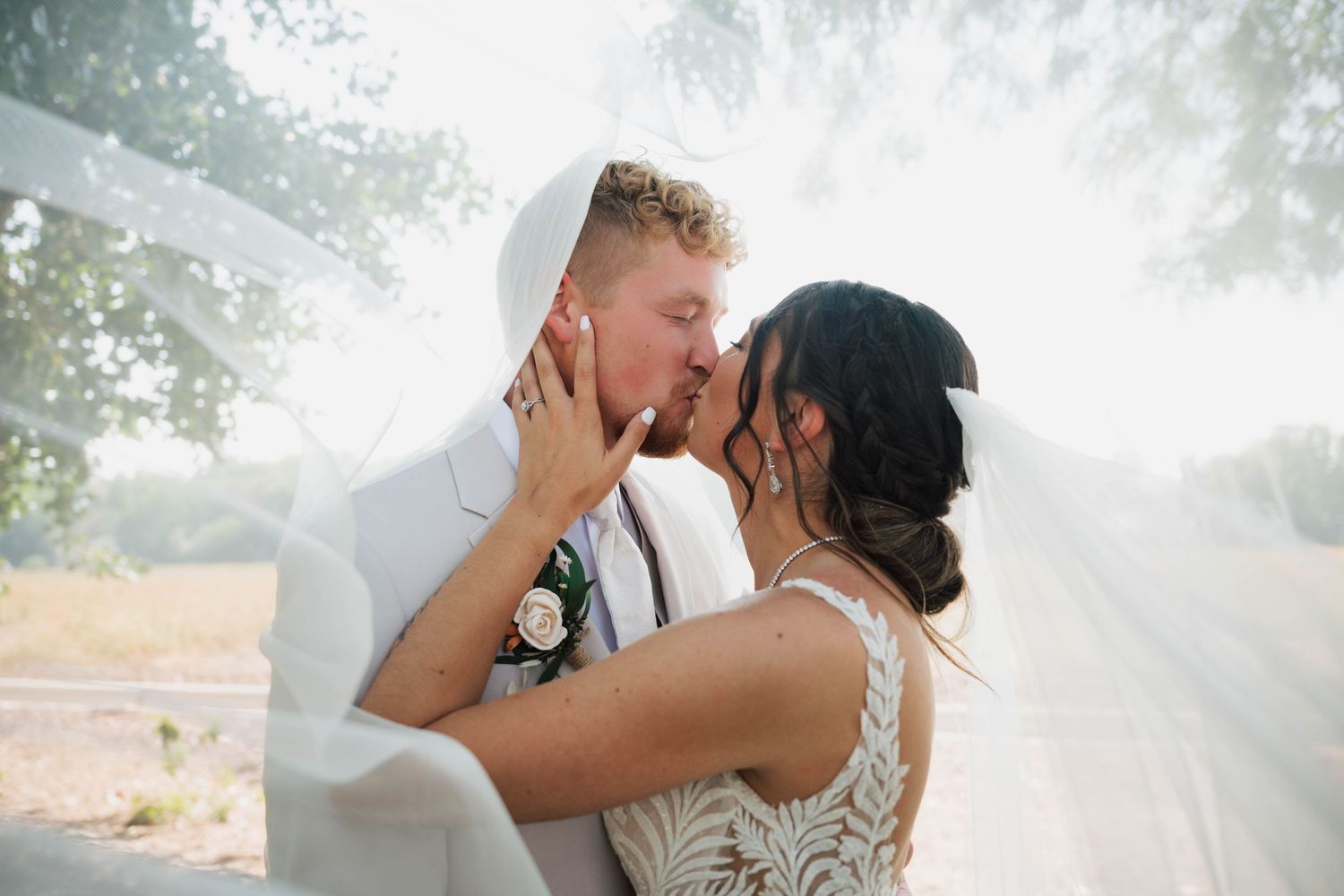 A bride and groom share a romantic kiss under a flowing white veil on their wedding day outdoors at deer flat ranch in nampa, idaho