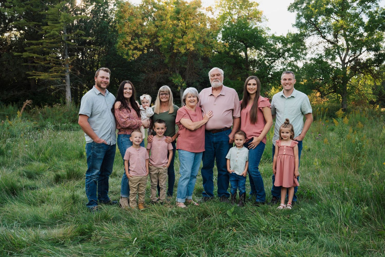 A large family group poses together outdoors in coordinated outfits during golden hour.