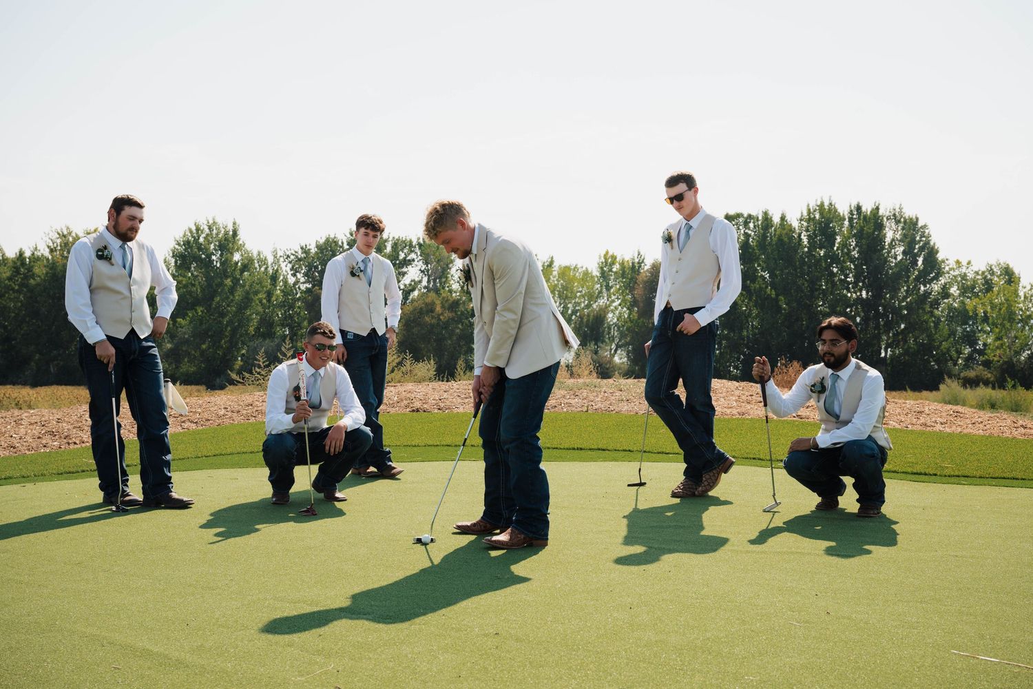 Groomsmen kneeling on golf green in playful wedding party photo.