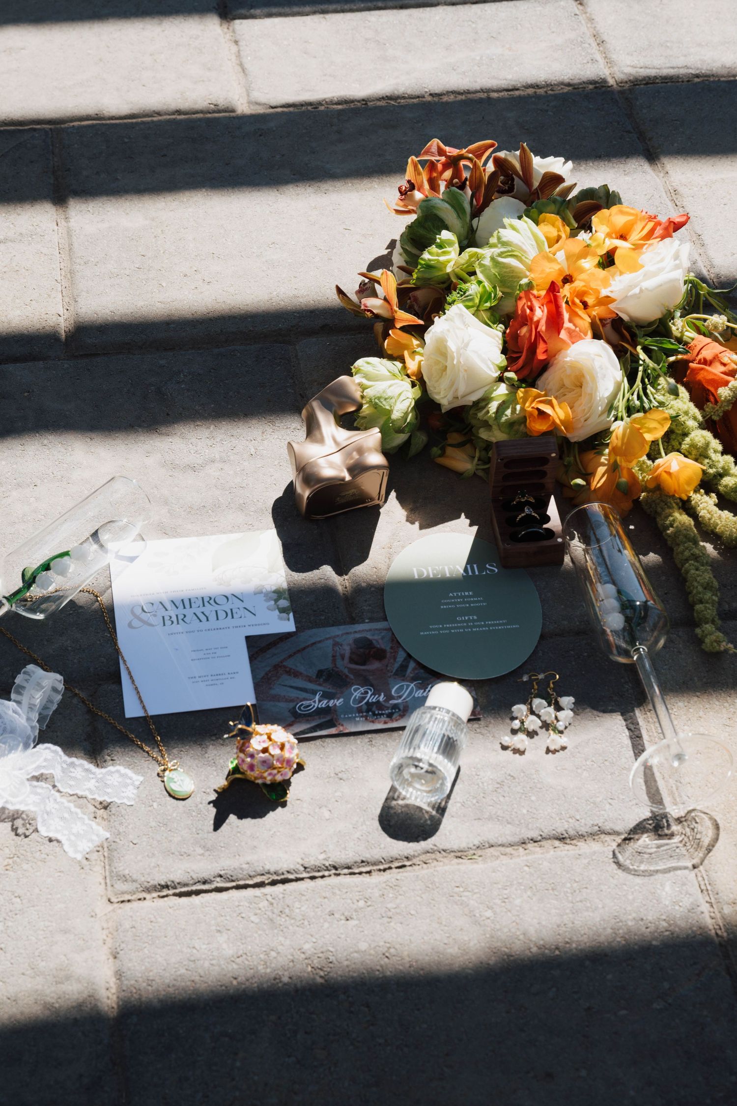 Wedding flat lay featuring colorful bridal bouquet, invitation suite, boutonniere, and accessories on stone steps.