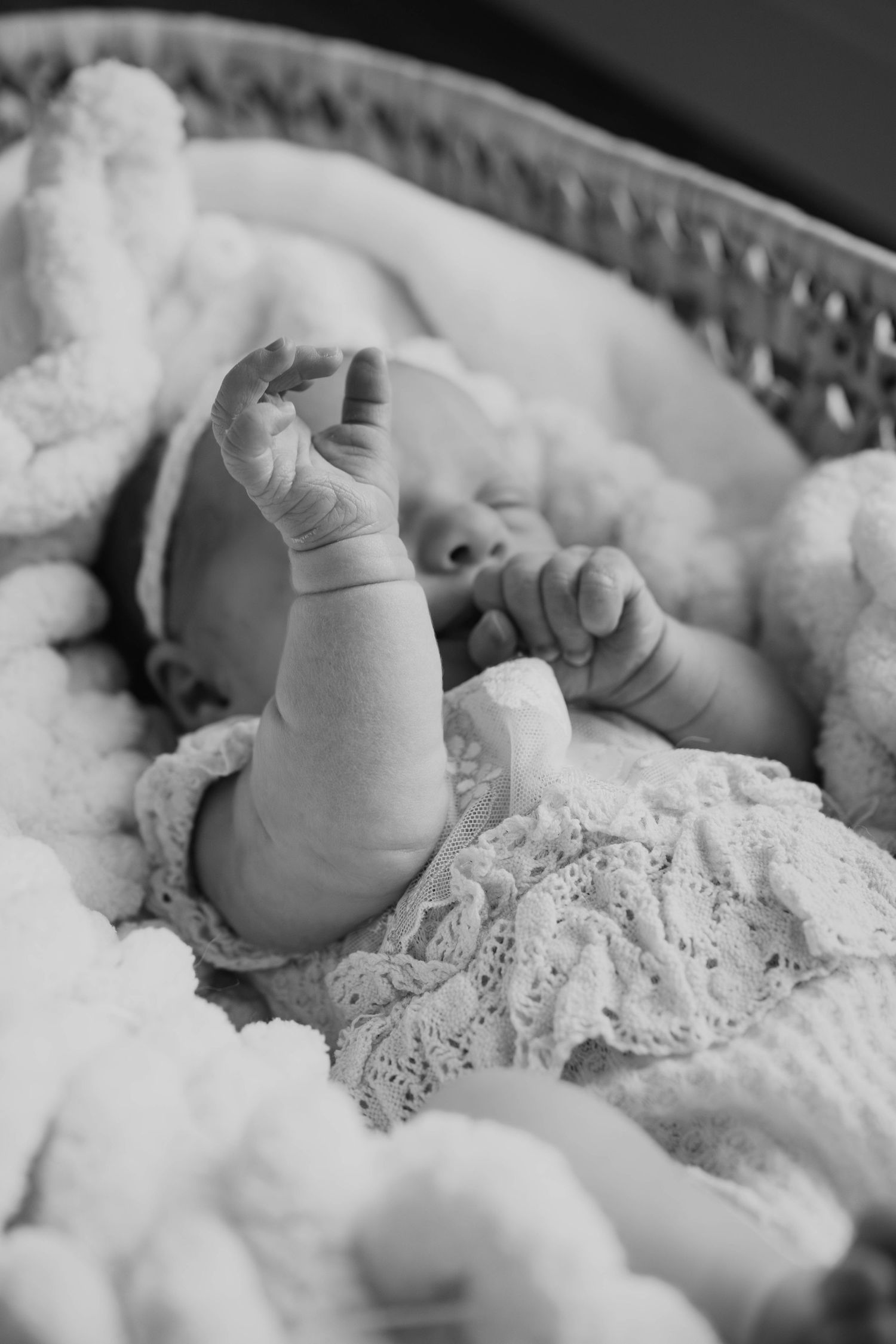 Black and white portrait of newborn baby resting on lace-trimmed bedding.