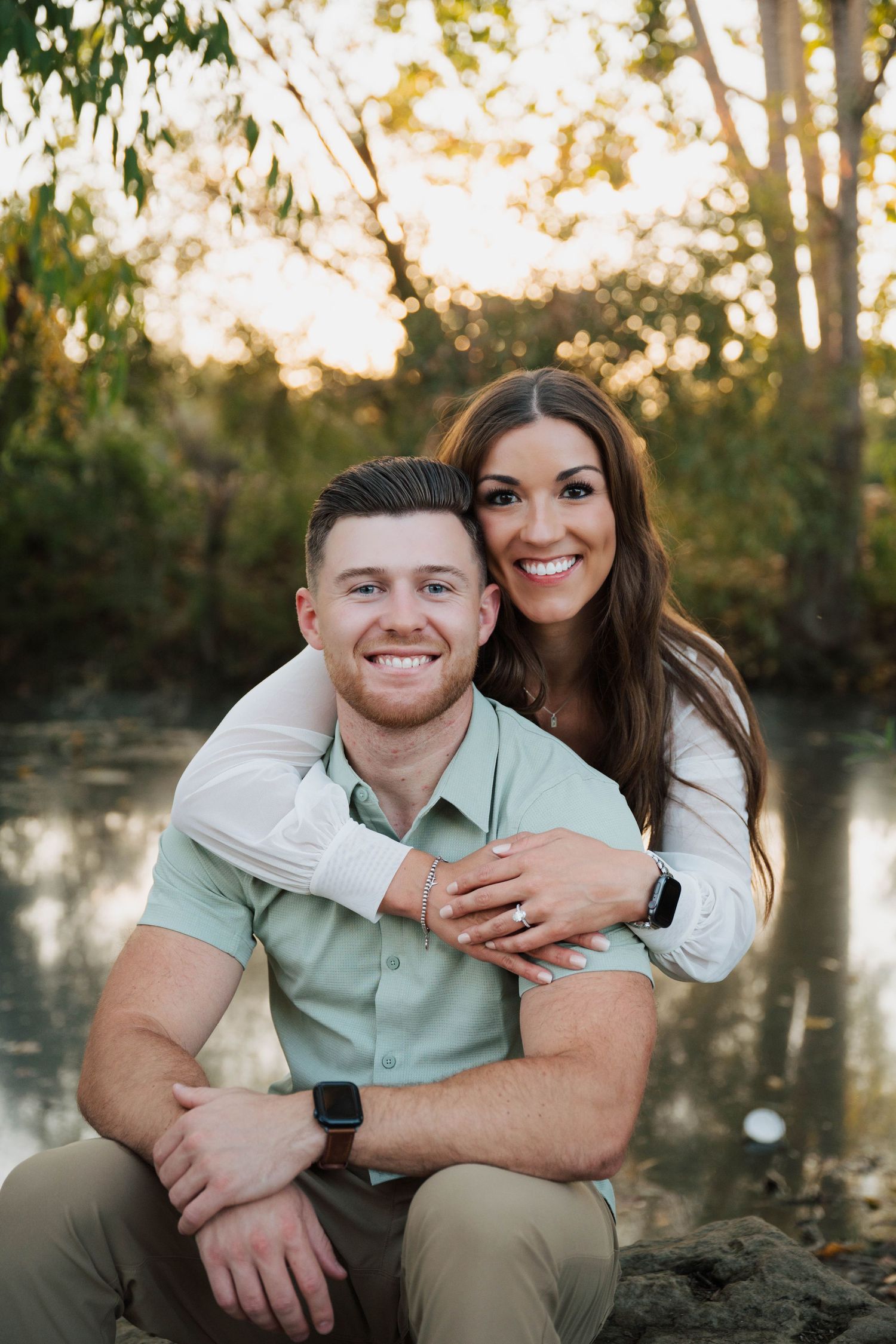 Couple in casual attire sharing intimate moments during a sunset photoshoot by a lake.