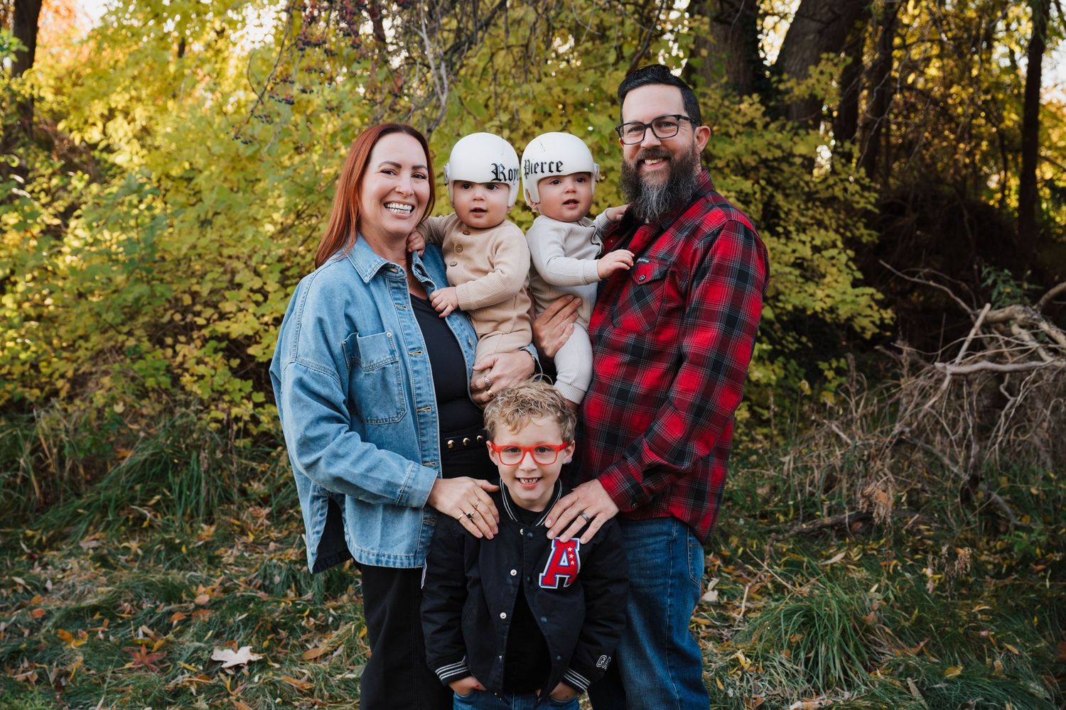 A family poses together in an outdoor autumn setting with golden foliage in the background.