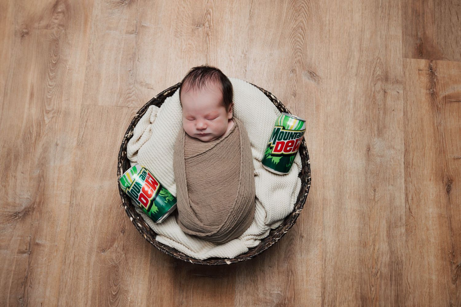 Overhead view of newborn photography setup with basket and props on wooden floor.