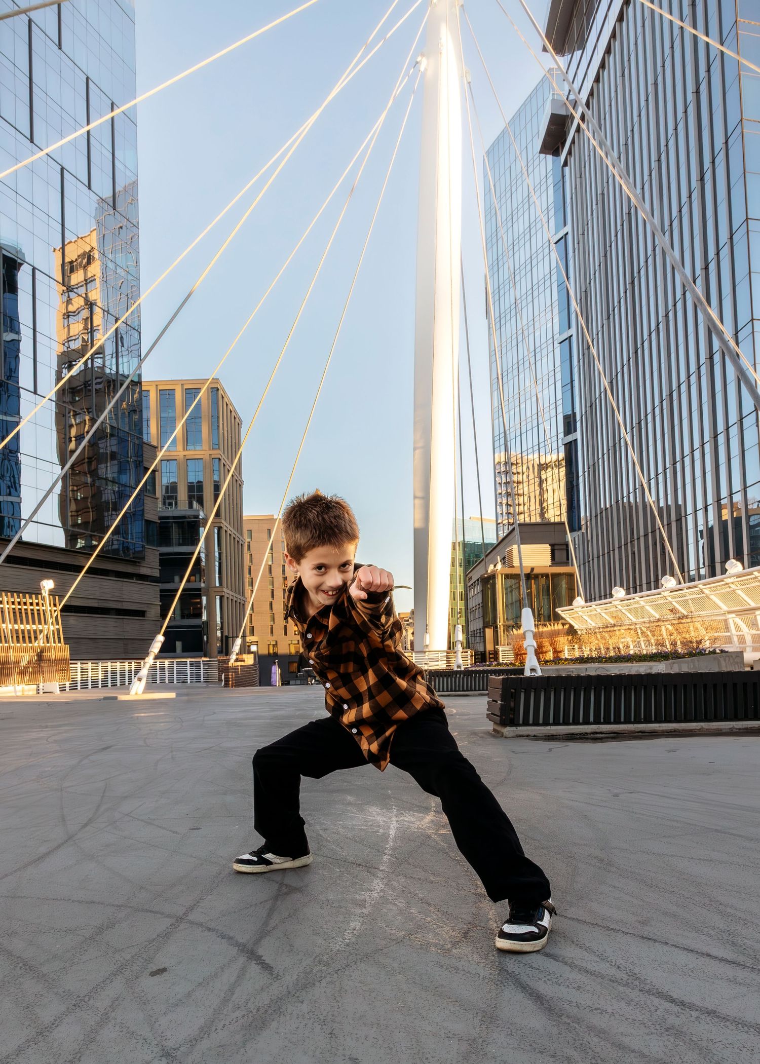 Portrait of child performing favorite super hero moves on bridge against modern architectural background with glass buildings.