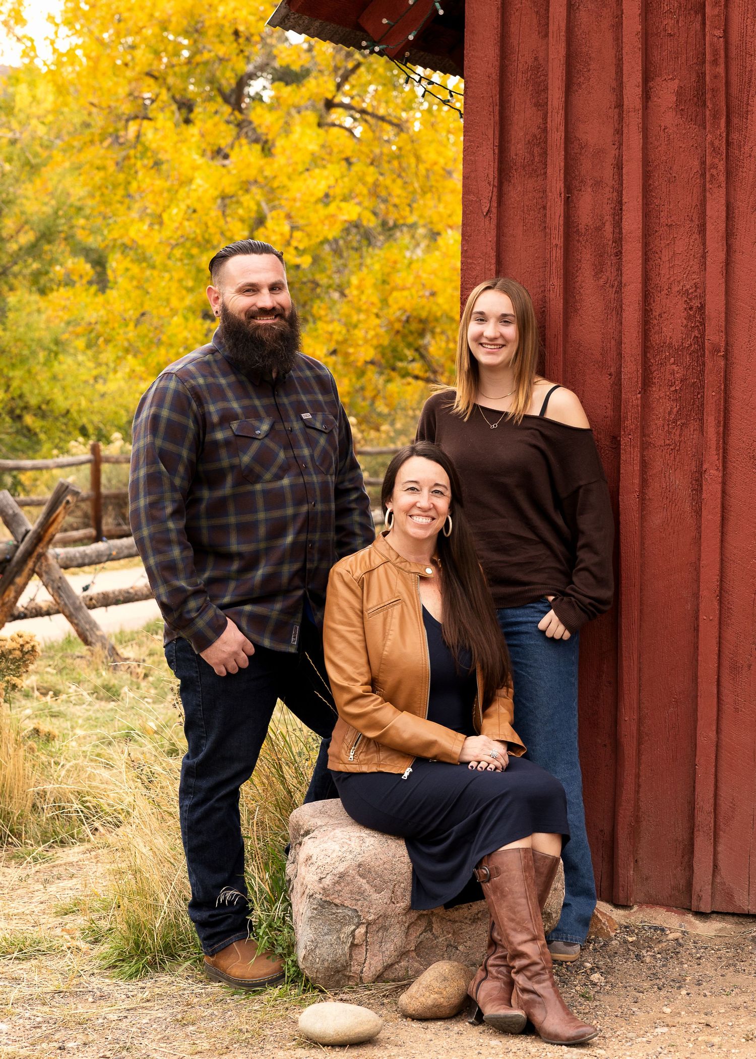 Family portrait photography session during peak fall colors near a red barn and rustic fence in Golden, Colorado