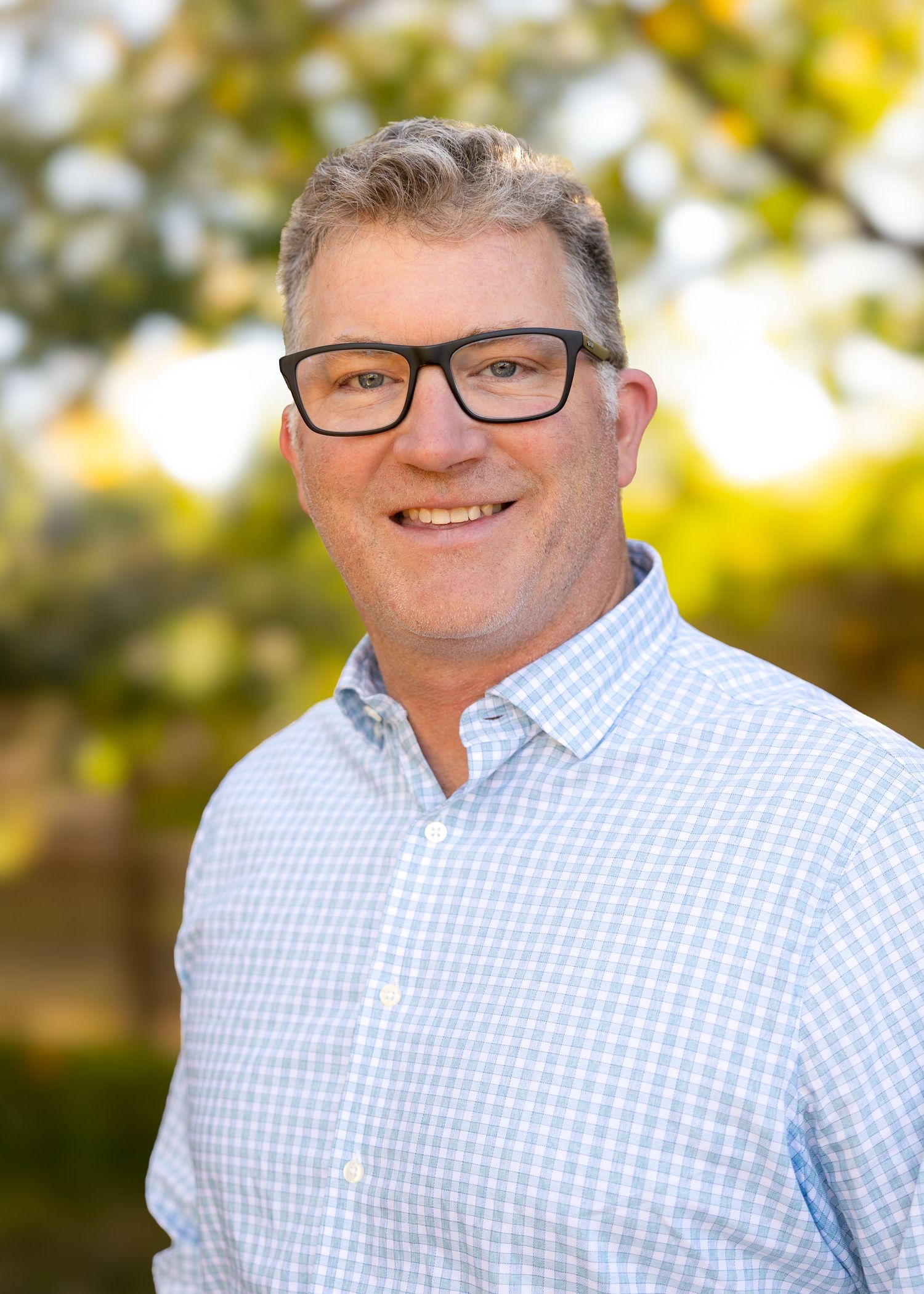 Professional headshots of corporate team member in checkered shirt and glasses against autumn background. Arvada, CO