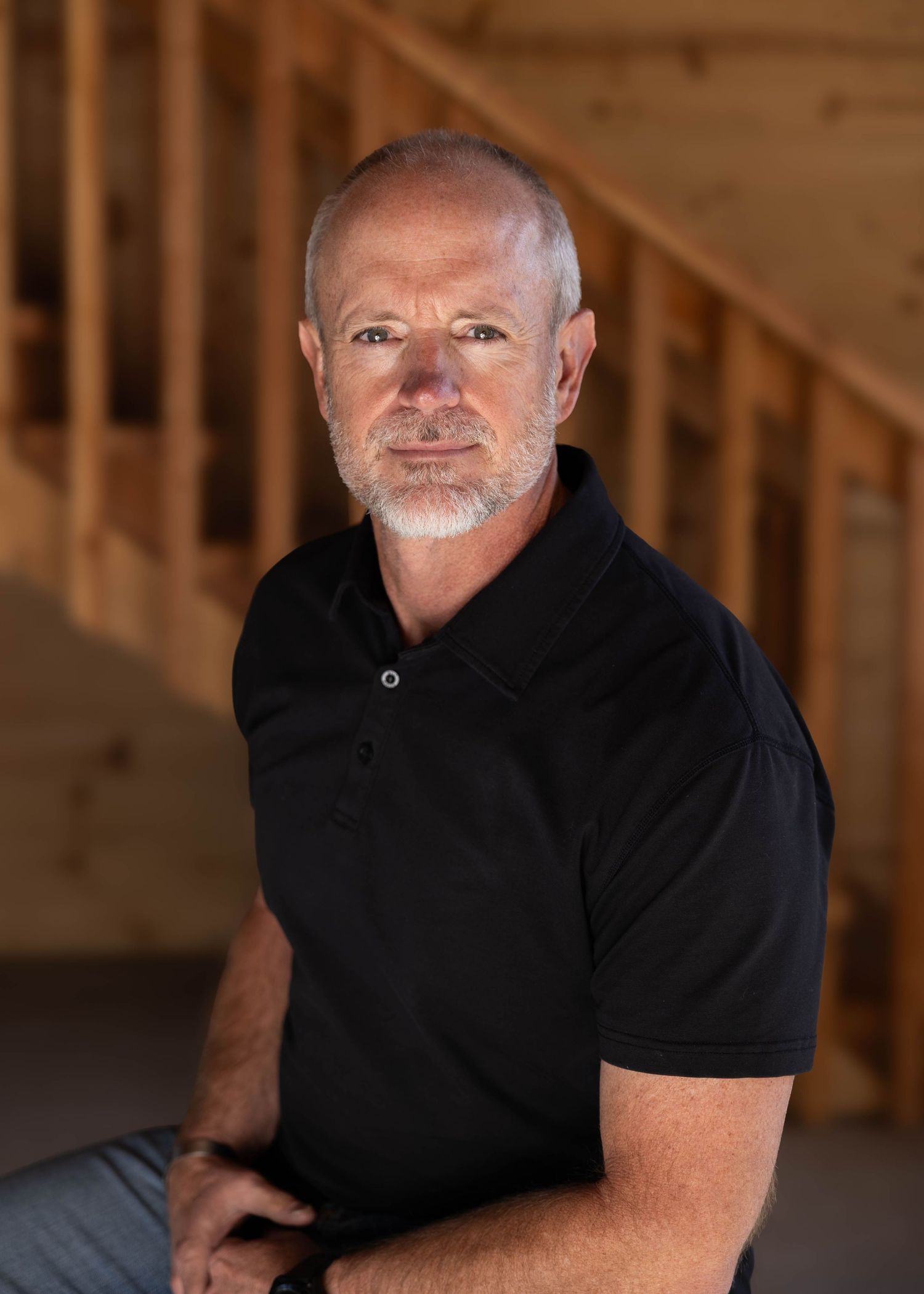 Professional headshot, Arvada, CO, of man in black polo shirt against wooden interior background using natural lighting.