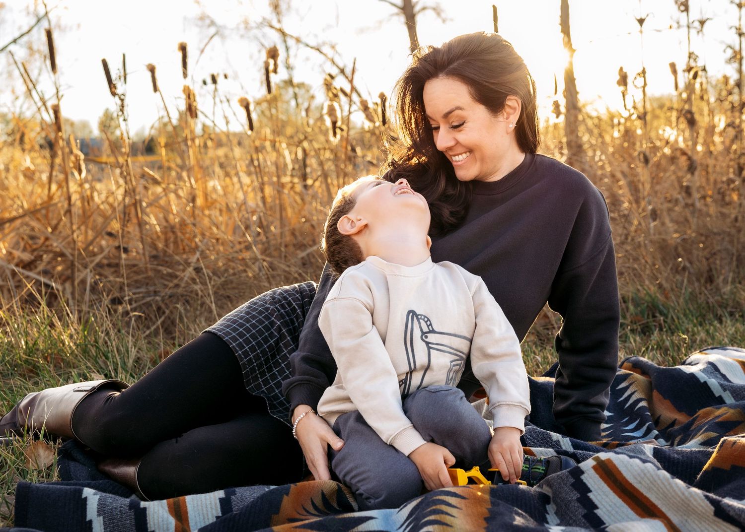 Natural light family photography by Wild Light Studio featuring a mother and son laughing together in a Colorado autumn field at golden hour