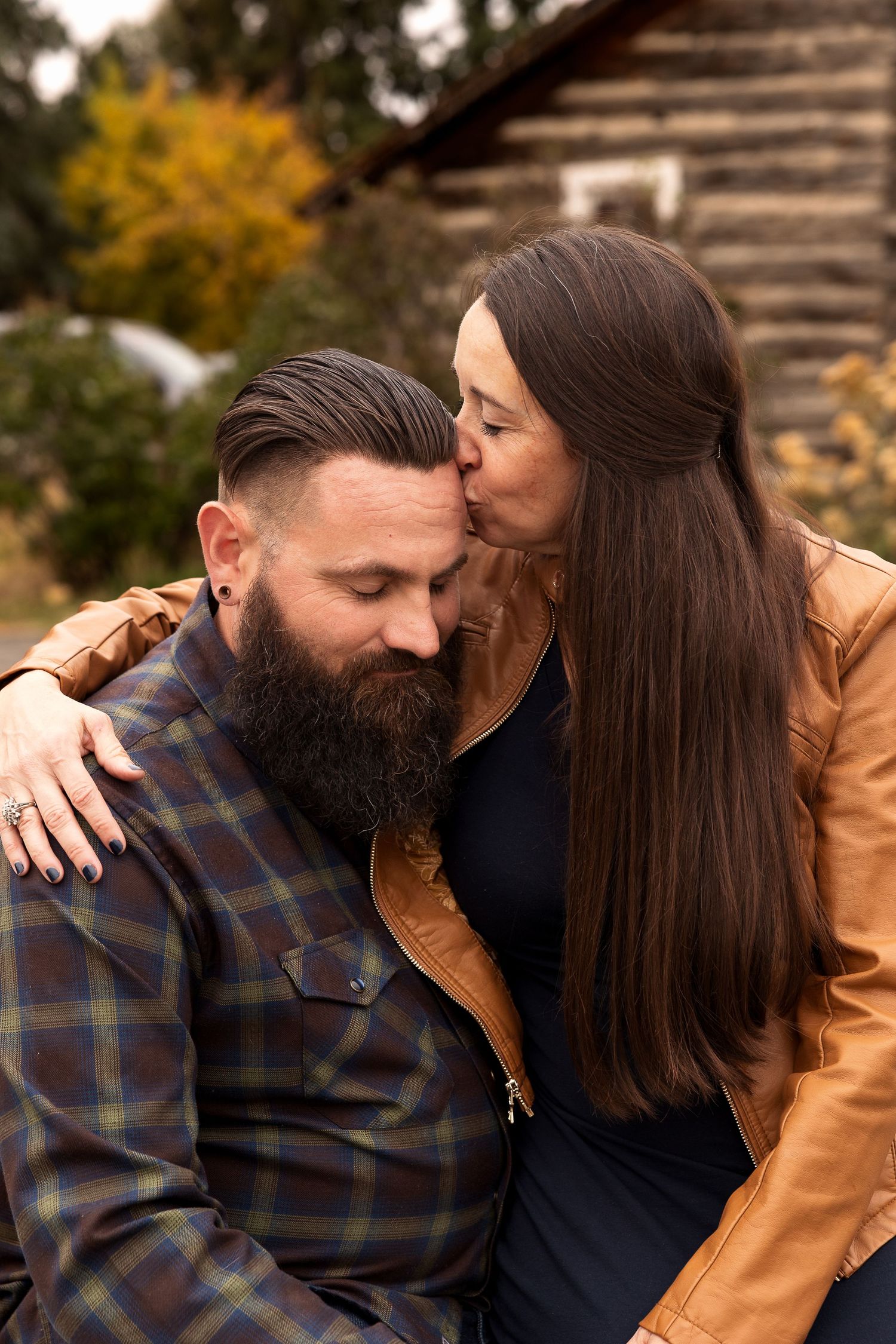 Intimate autumn portrait of a couple embracing near a rustic cabin in Golden, Colorado with fall foliage in the background.