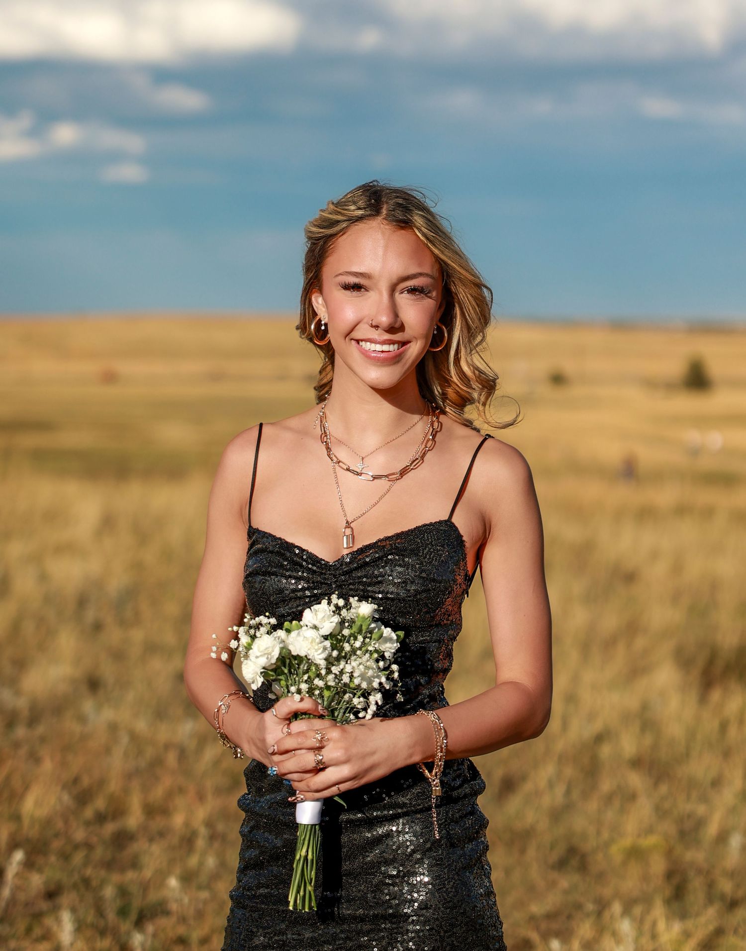 Portrait of Homecoming girl in black dress stands in golden field during sunset in Boulder, CO