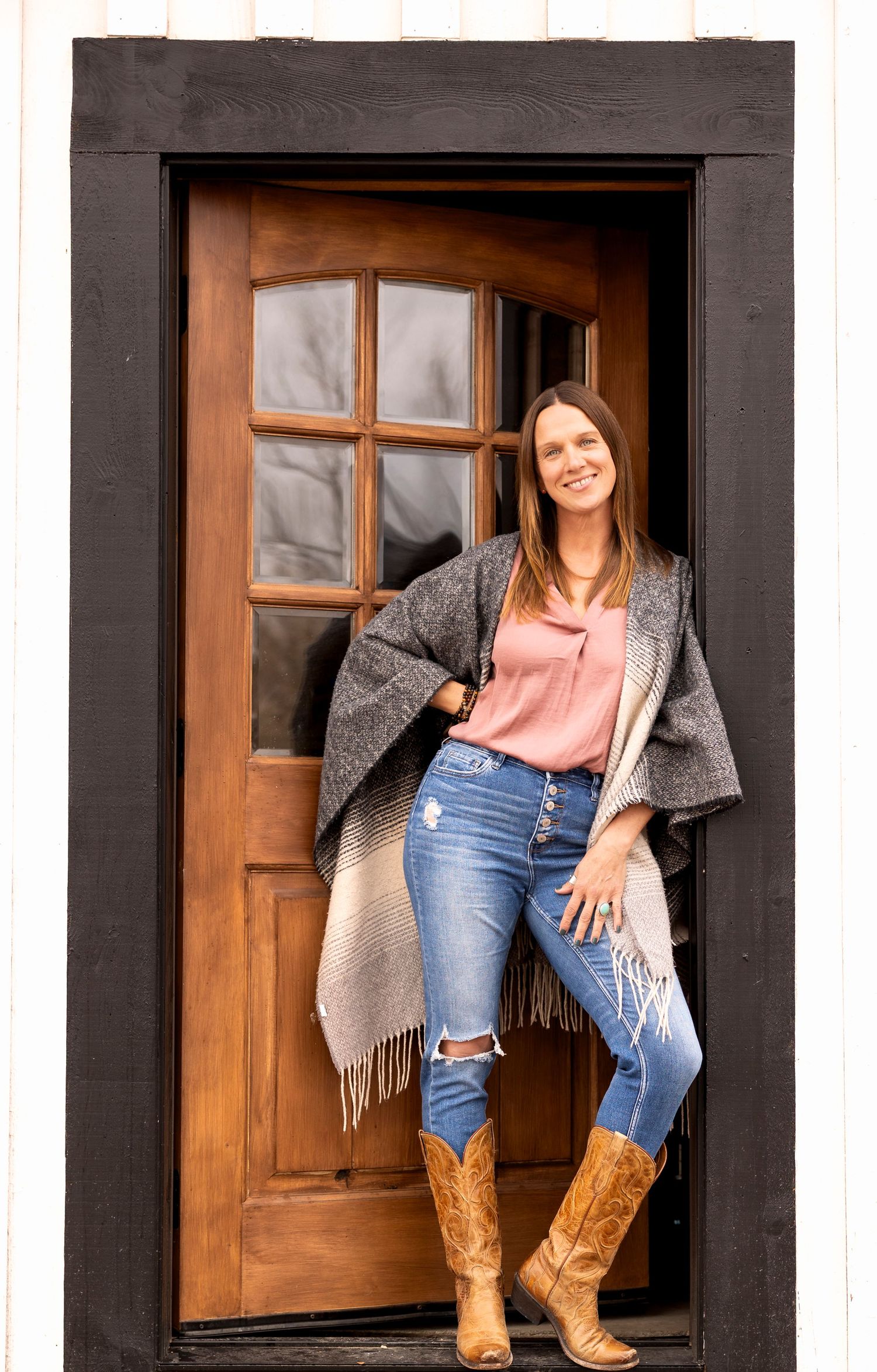Self portrait by Wild Light Studio photographer wearing distressed jeans sitting in rustic doorway of barn with cowboy boots. Arvada, CO