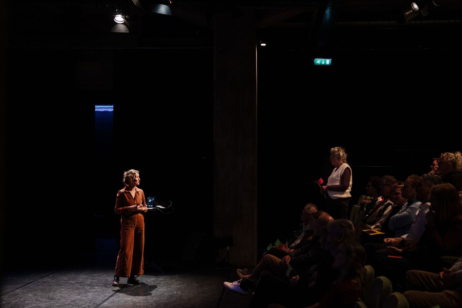 Two performers on stage with audience watching in darkened intimate theater venue.