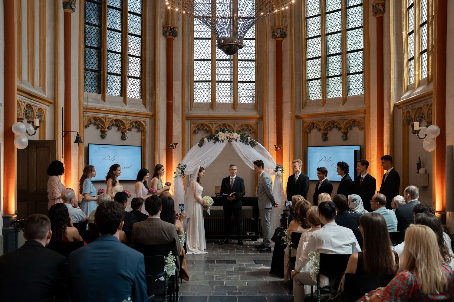 Wedding ceremony in an elegant hall with stained glass windows and floral arch altar.