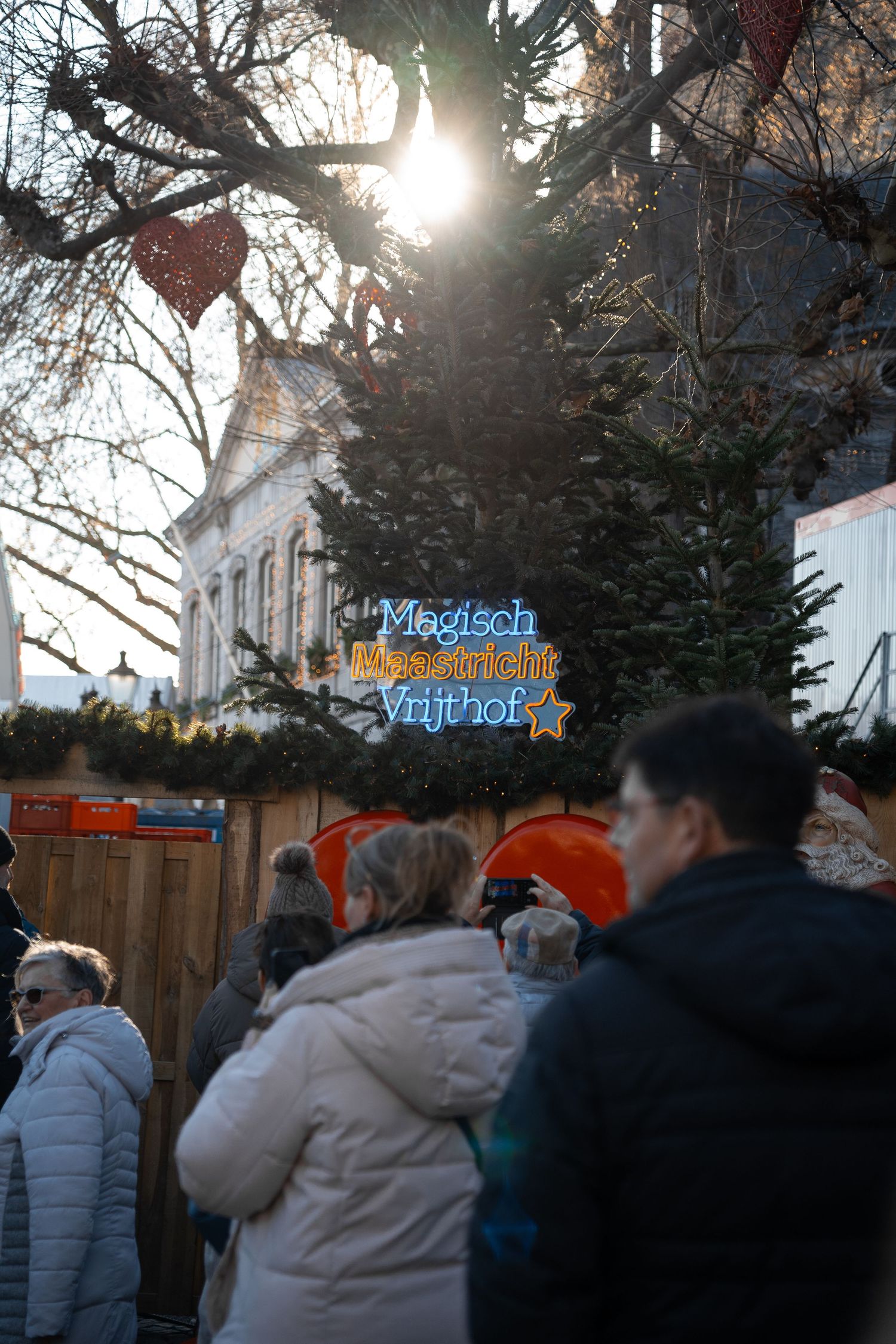 Crowd gathered around a glowing Magisch Maastricht Vrijthof Christmas market sign at sunset.