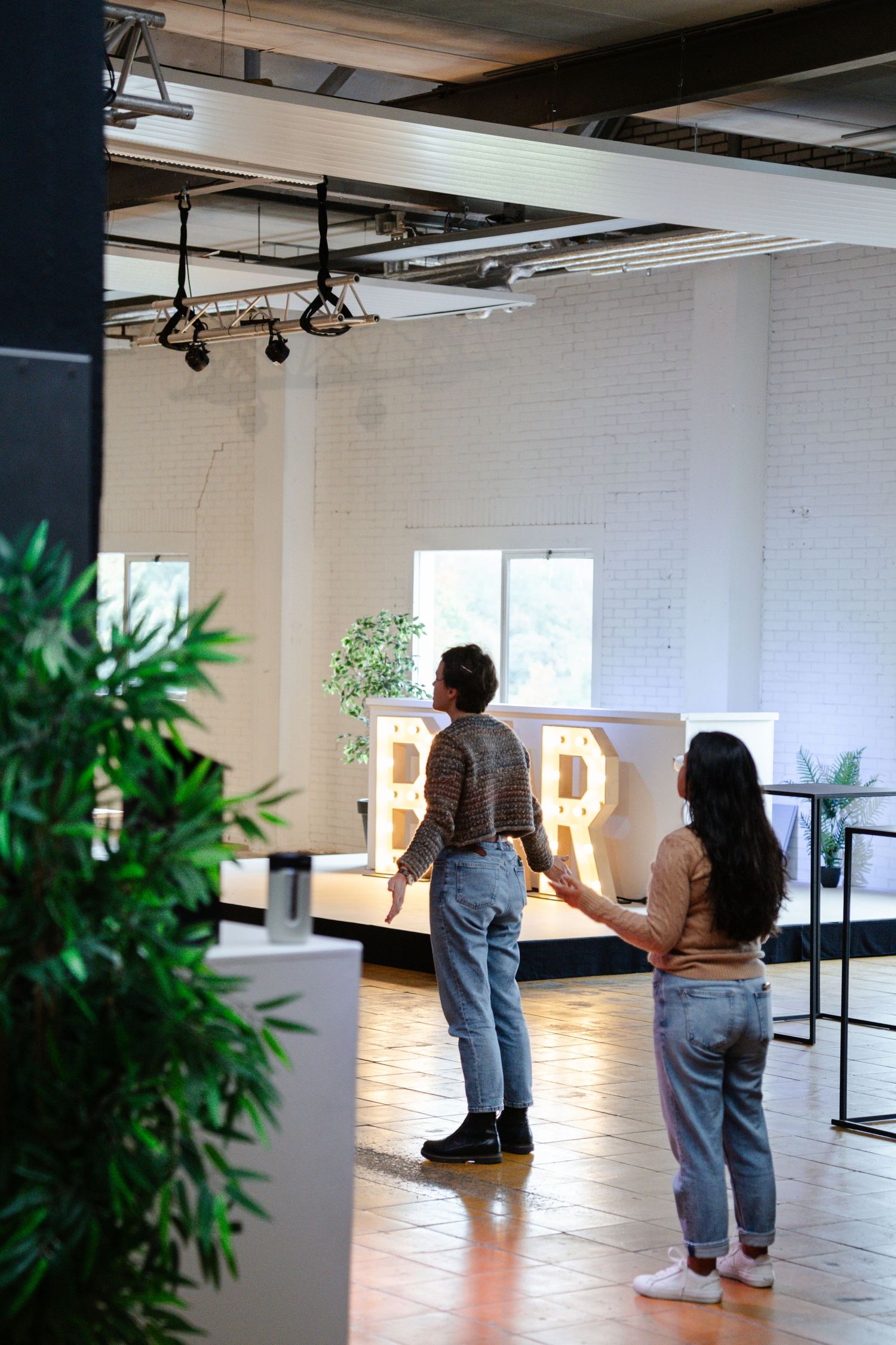 Two people holding hands view illuminated letter R decorations in a modern industrial event space.