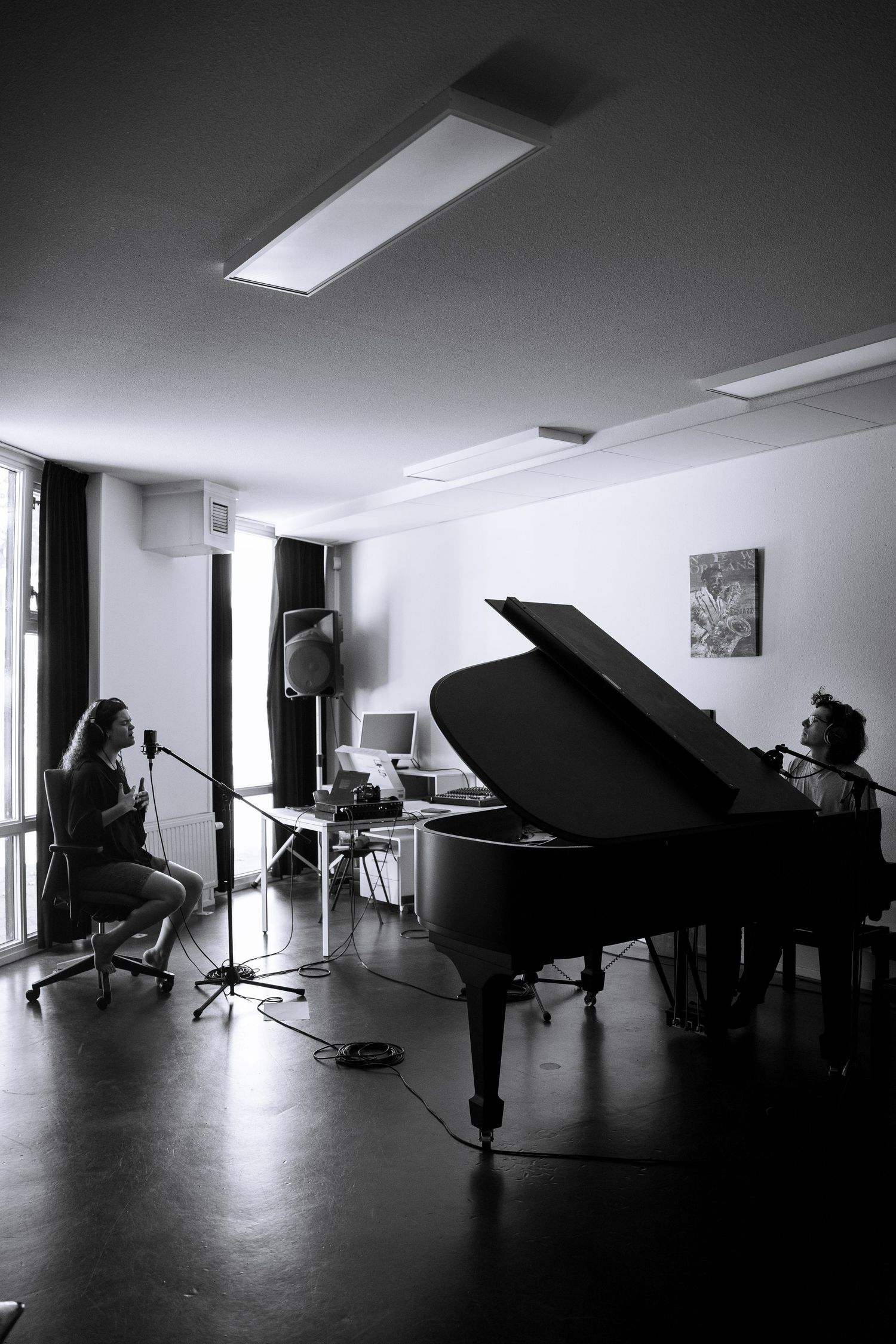 Black and white photo of two musicians recording in a studio with a grand piano and microphone setup.