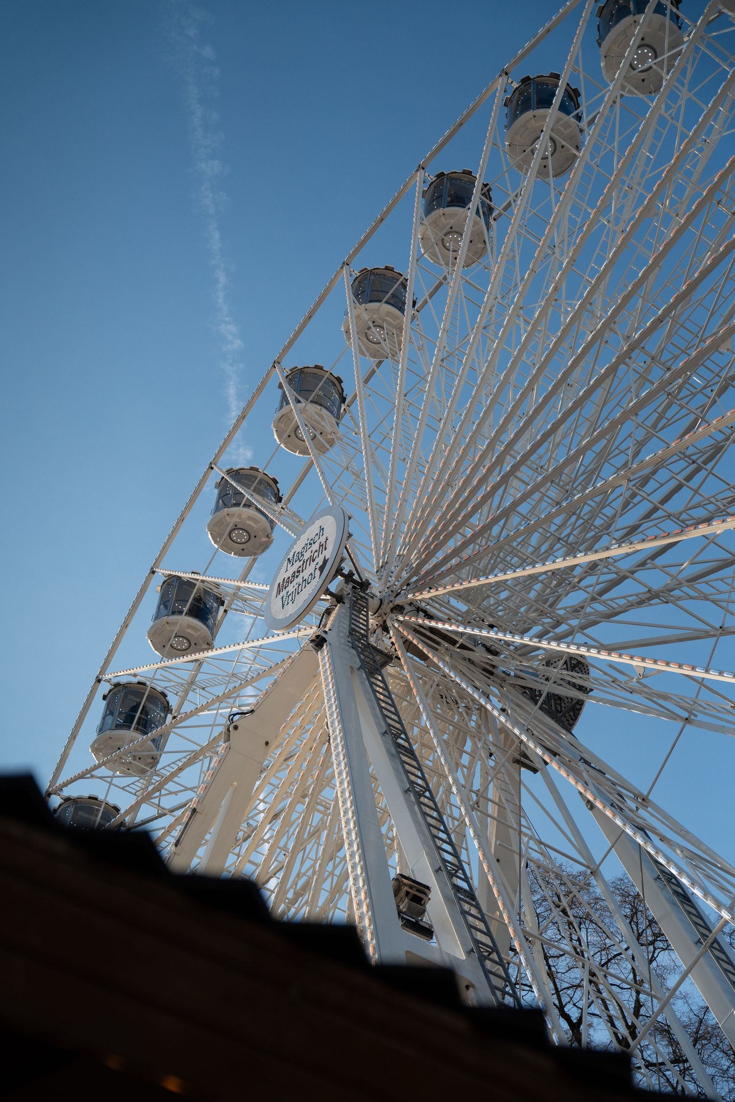 Low-angle view of a large white Ferris wheel against a clear blue winter sky.