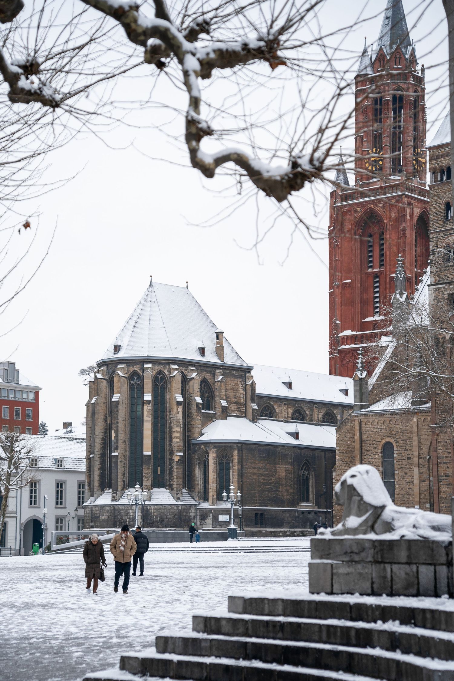 Snow-covered medieval church and cathedral square with visitors walking in a European winter cityscape.