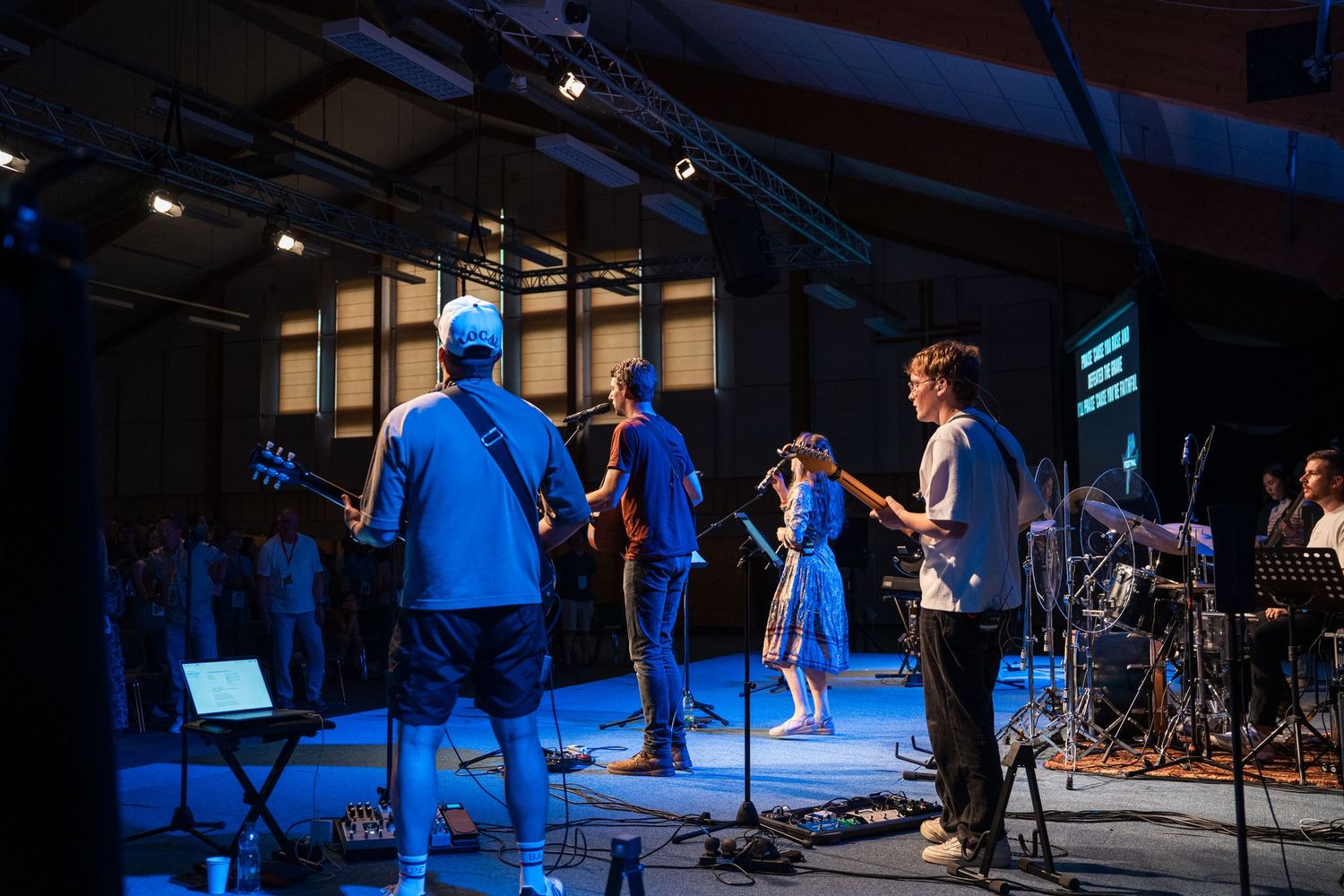 Live band performing on stage under blue lights at indoor venue evening concert.