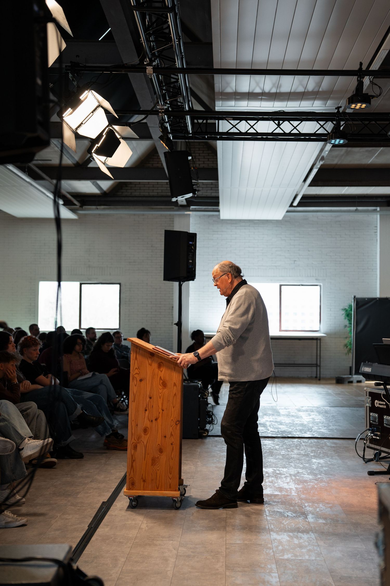 Speaker presenting at a podium on stage before a seated audience in a modern industrial event space.