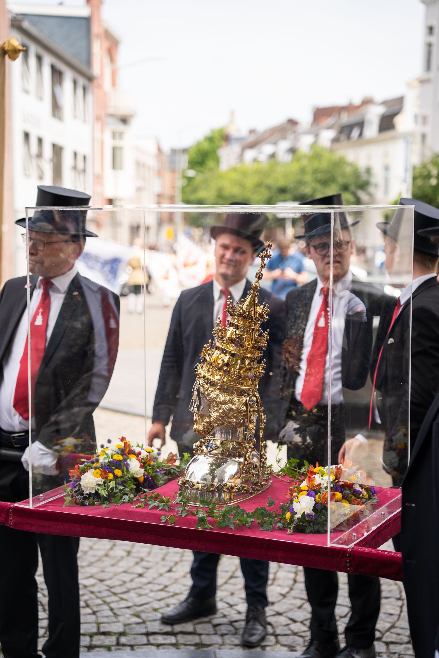 Men in black suits display ornate golden religious relic in glass case outdoors.