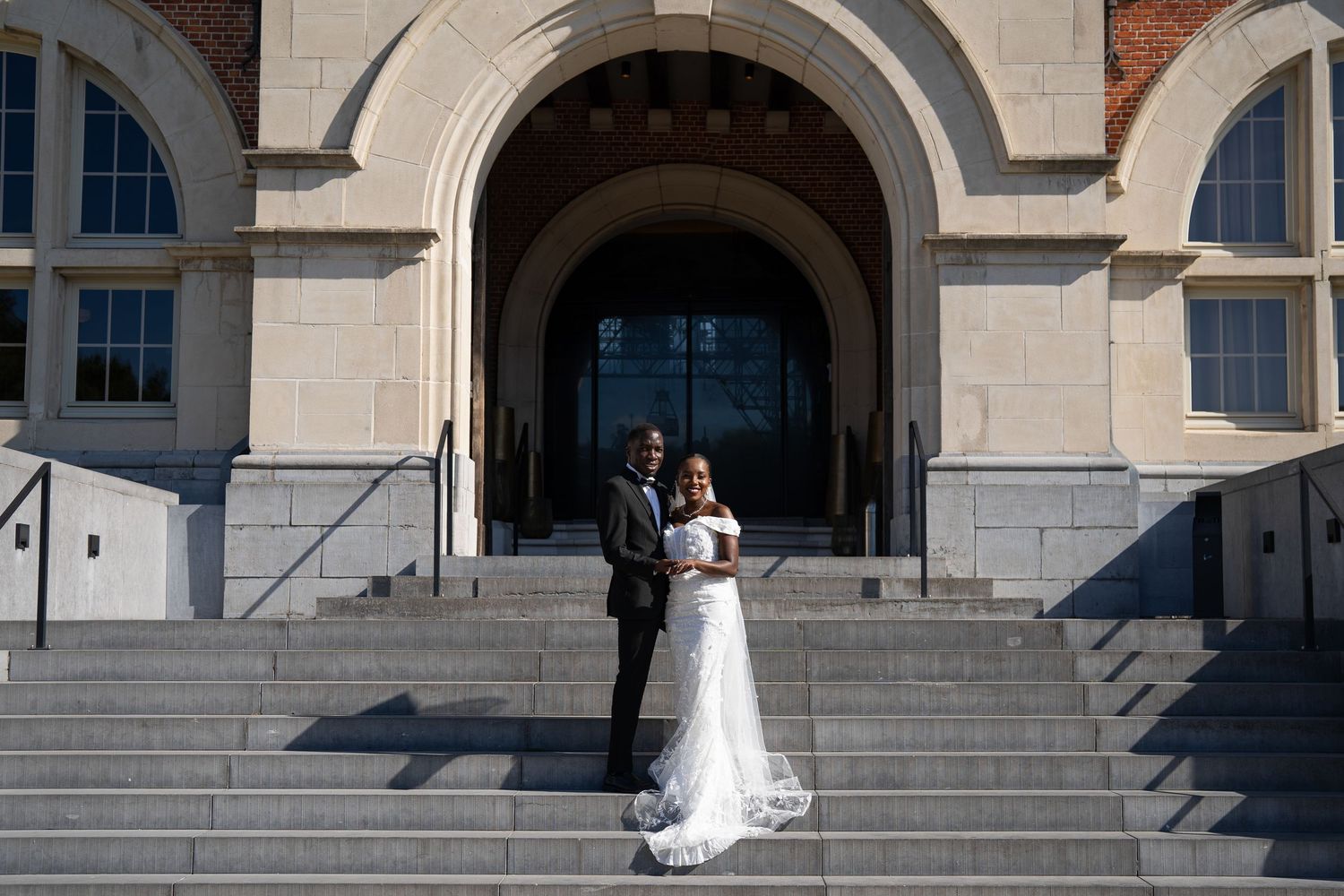 Bride and groom posing on steps of grand stone building with arched entrance.